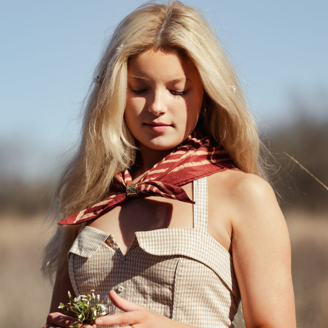 Woman with a red scarf around her neck, standing outdoors with a blurred background