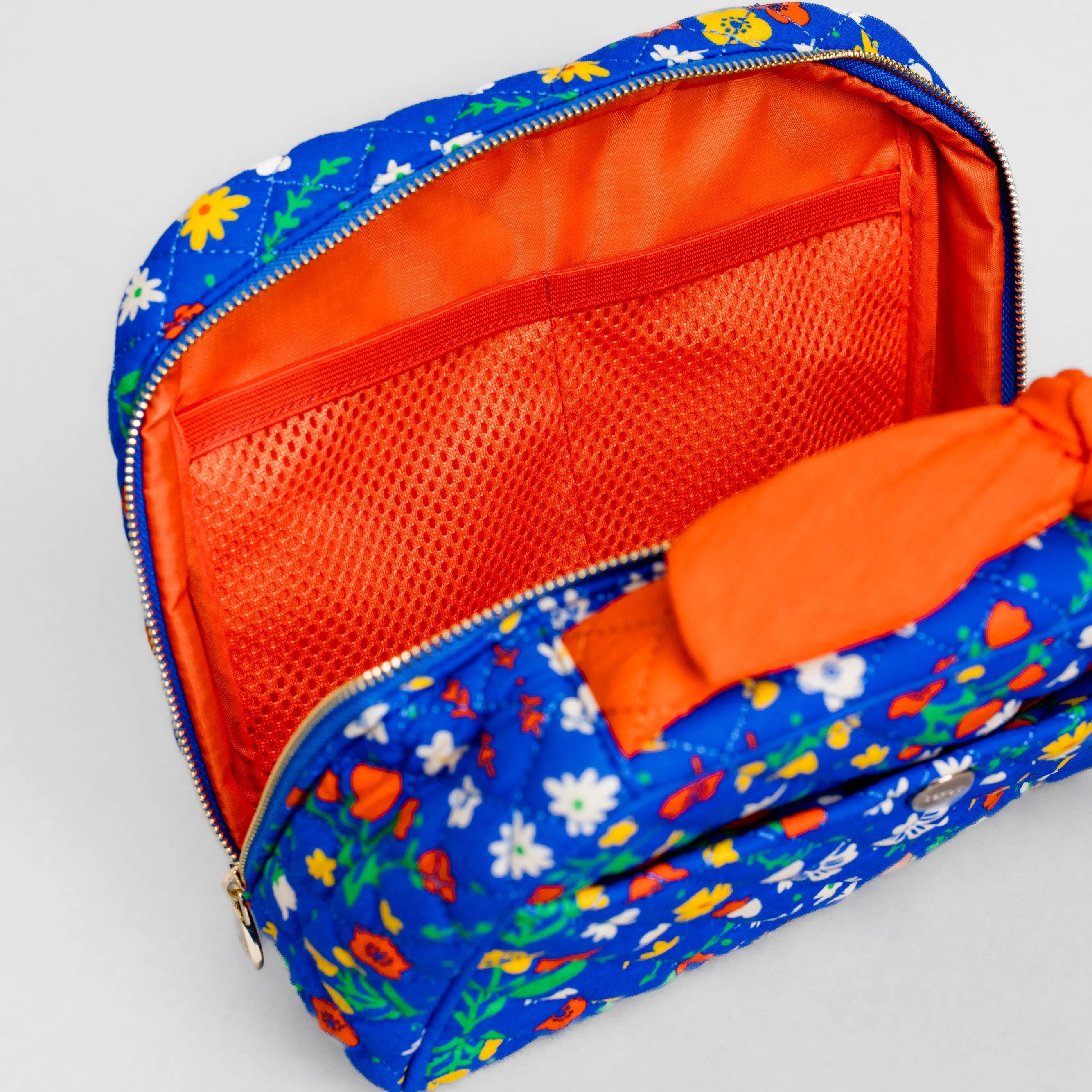 A blue floral zippered pouch with a bright orange mesh interior and matching orange fabric lining, shown open on a light gray background.