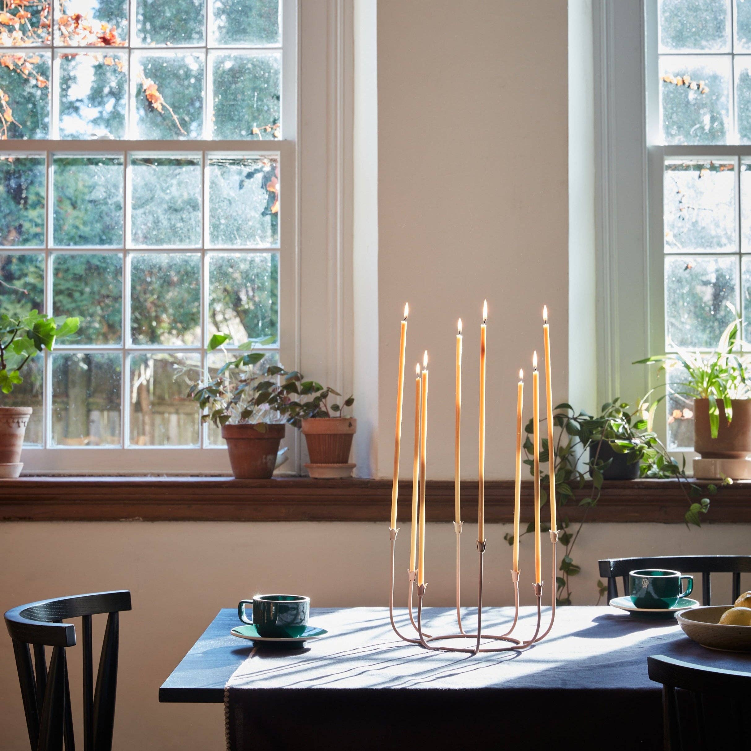 Candle holder with lit candles on a table in a room with large windows and plants.