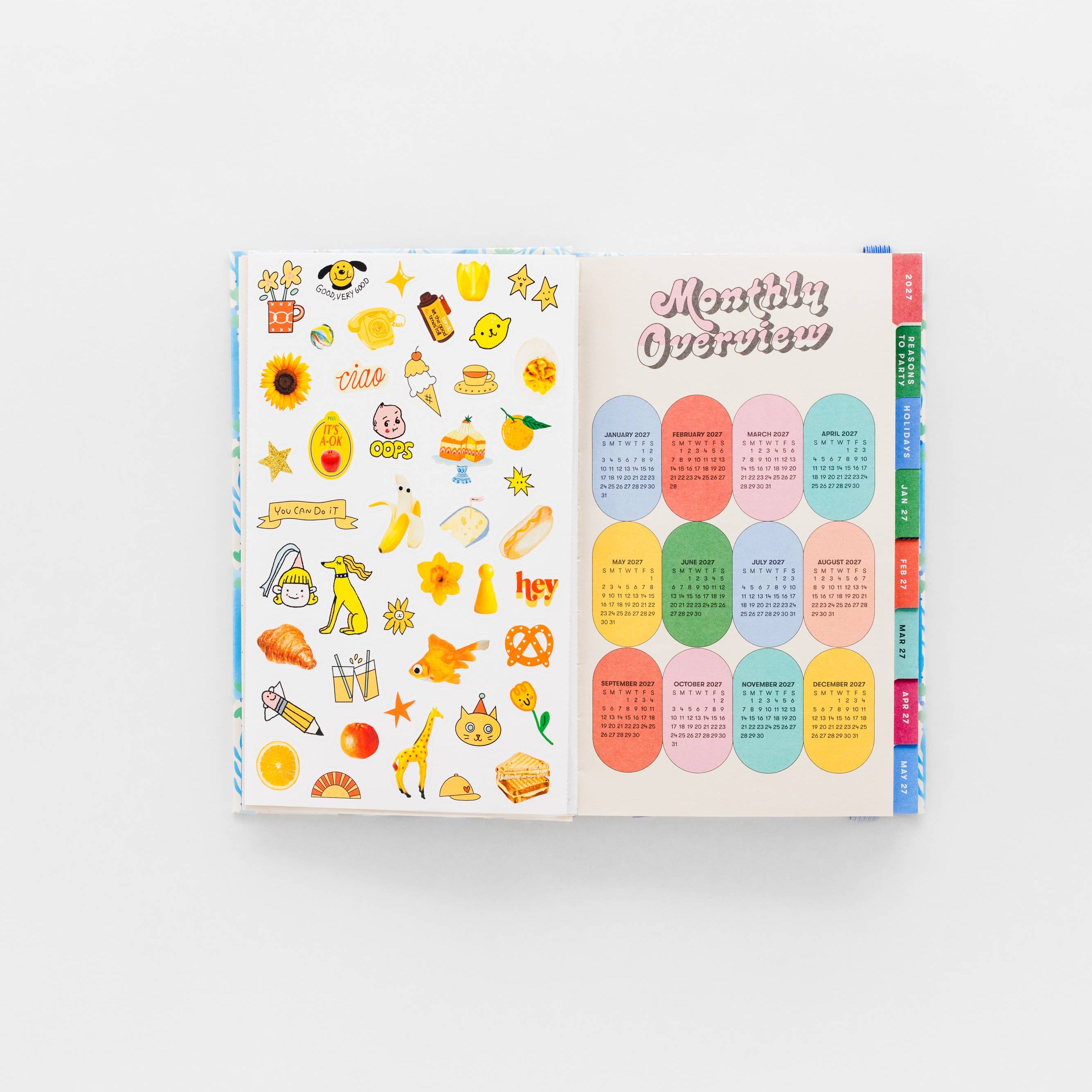 An open sticker or planner insert book on a white background, showing colorful food-themed stickers on one page and pastel oval monthly quote stickers on the other.