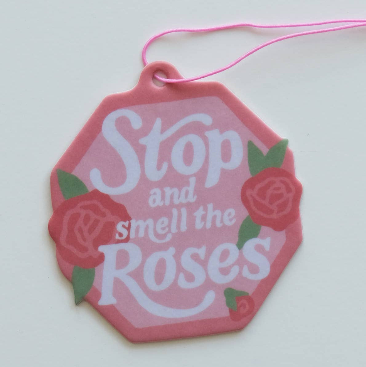 Pink hexagonal air freshener with 'Stop and smell the Roses' text and roses on a white background