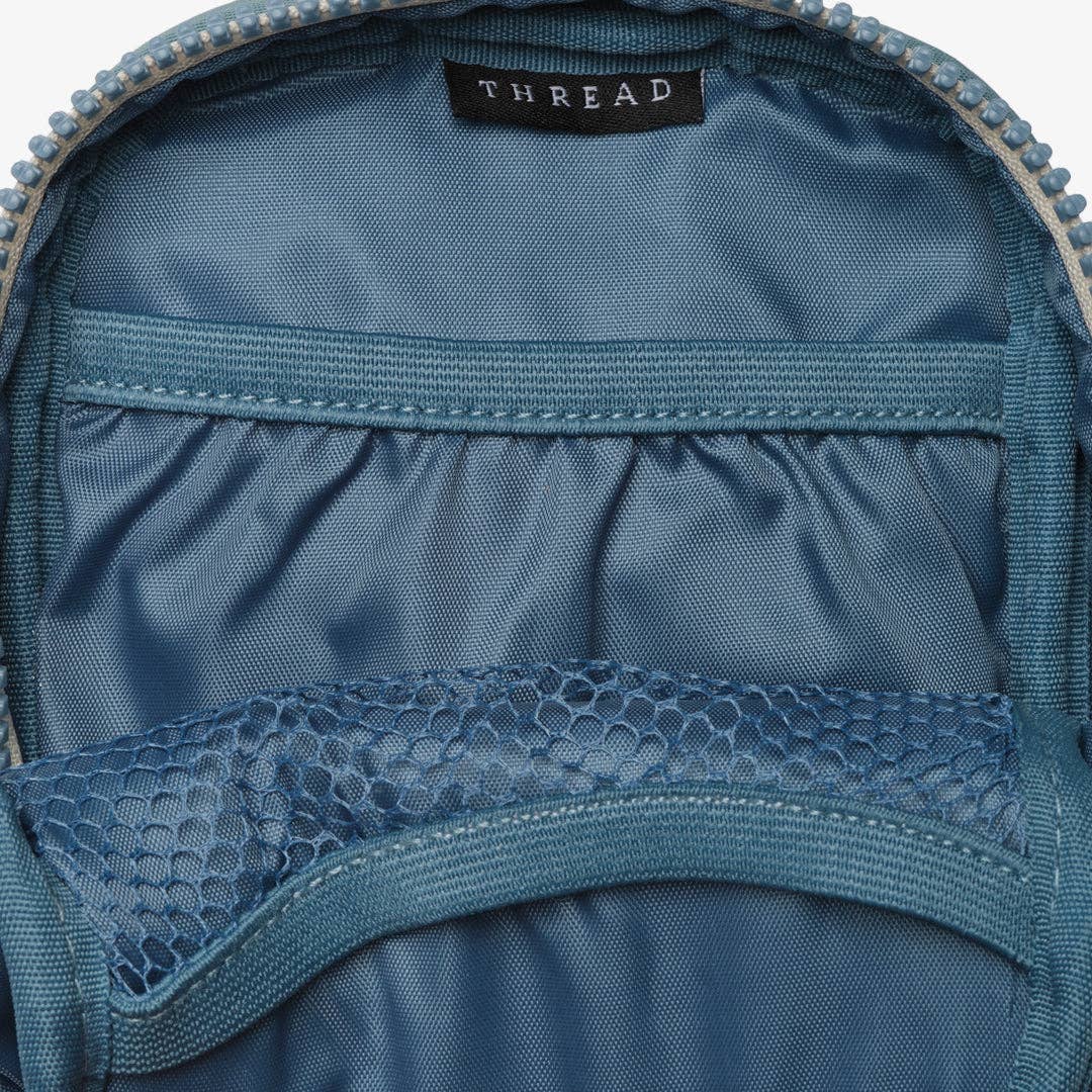 Close-up of the interior of a blue backpack, showing the lining, zipper, elastic pocket, and a black brand label reading THREAD.