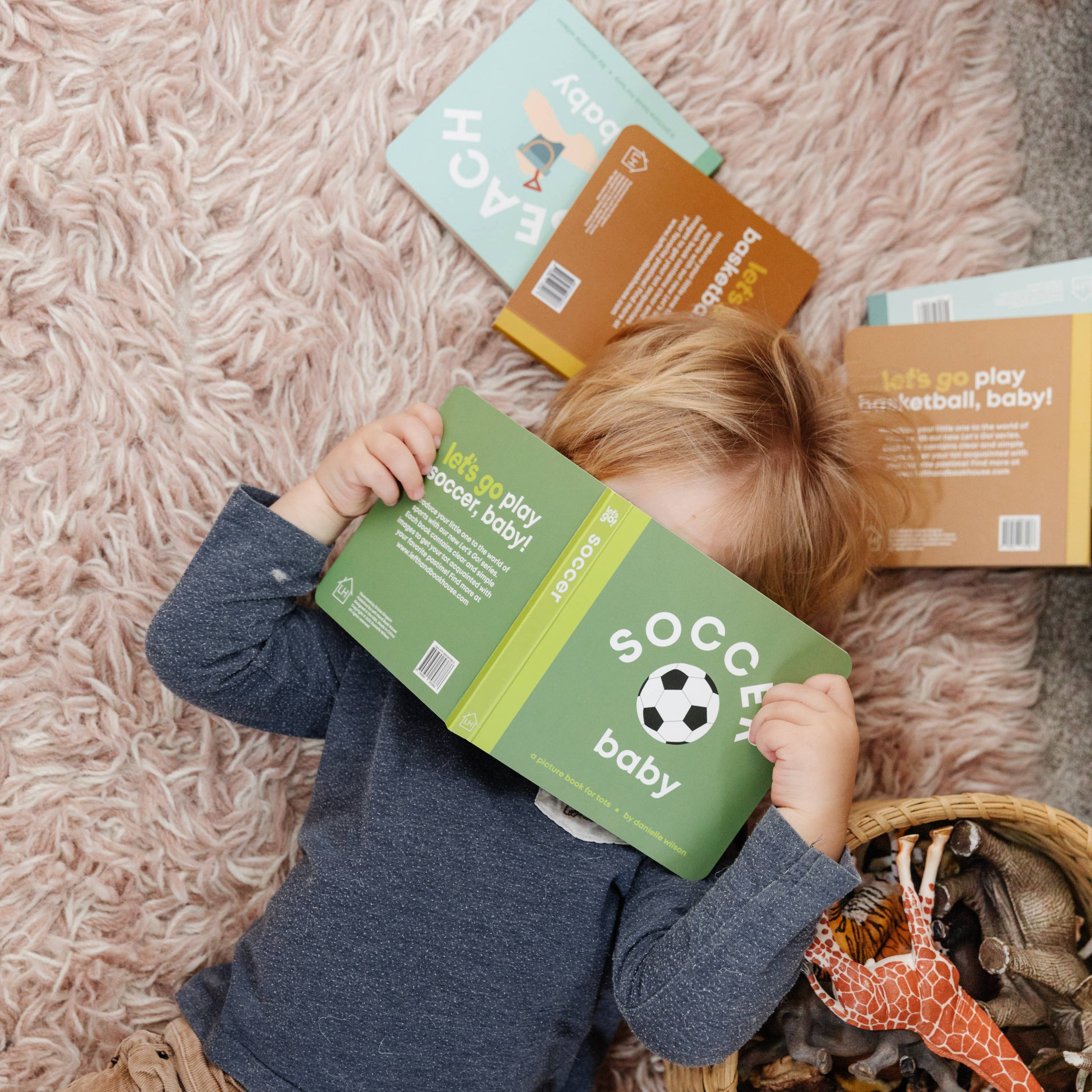 Child playing with books and toys on a pink carpet