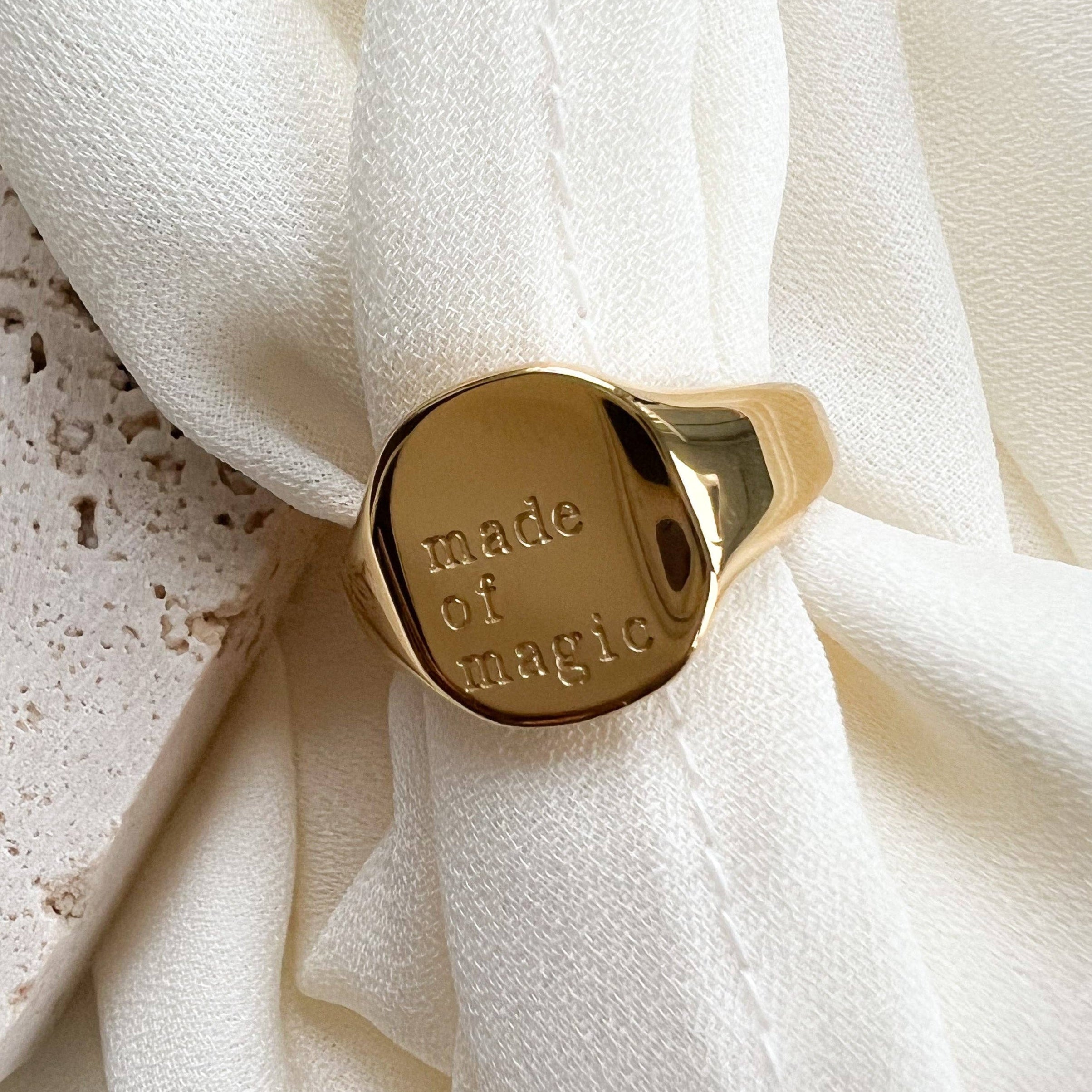Gold ring with 'made of magic' engraving on a white fabric background