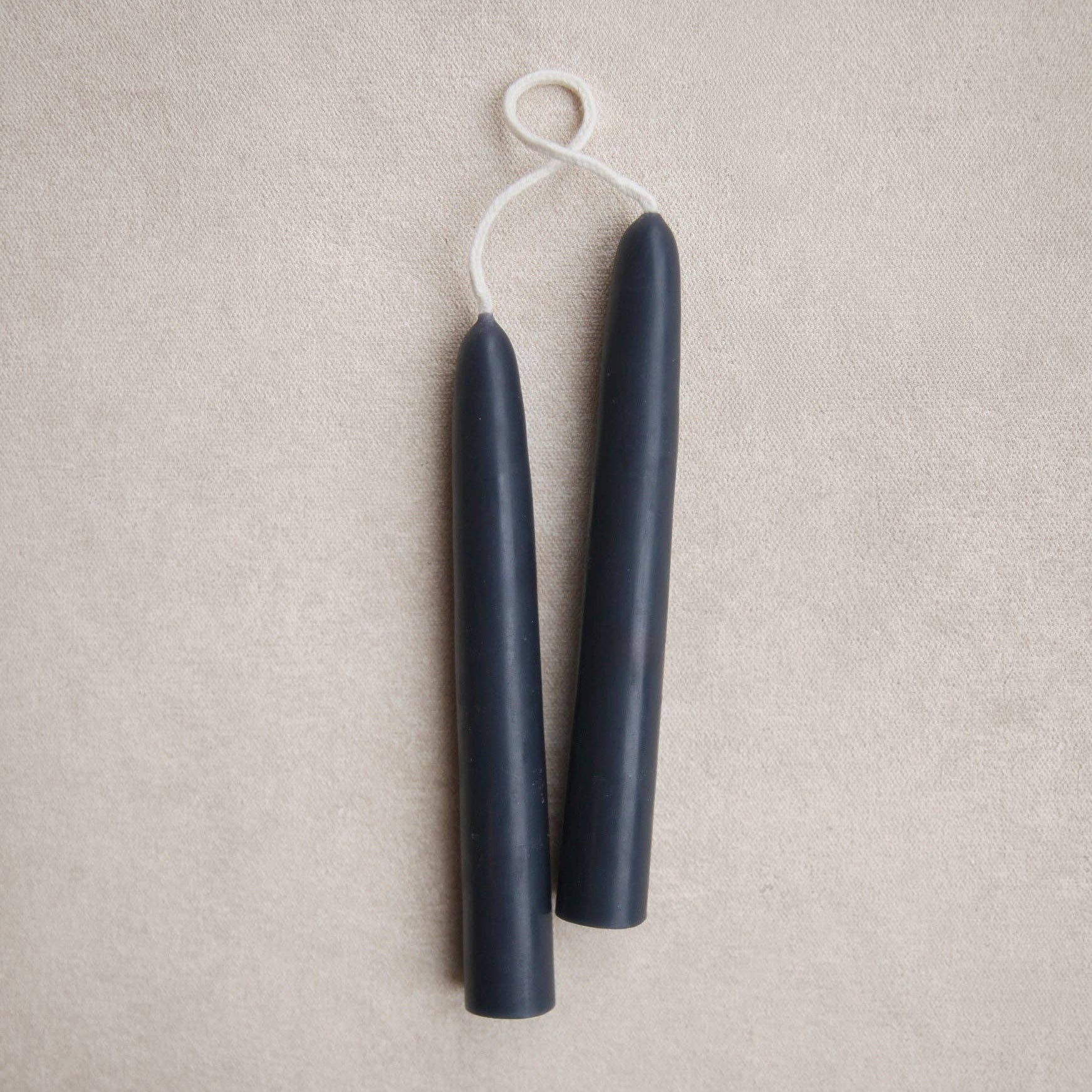 Two dark blue candles on a beige fabric background, ink color