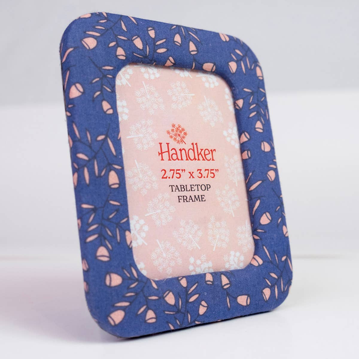 A square fabric picture frame with a blue floral patterned border and a light pink center insert, photographed on a clean white background. The insert reads 'Handker 2.