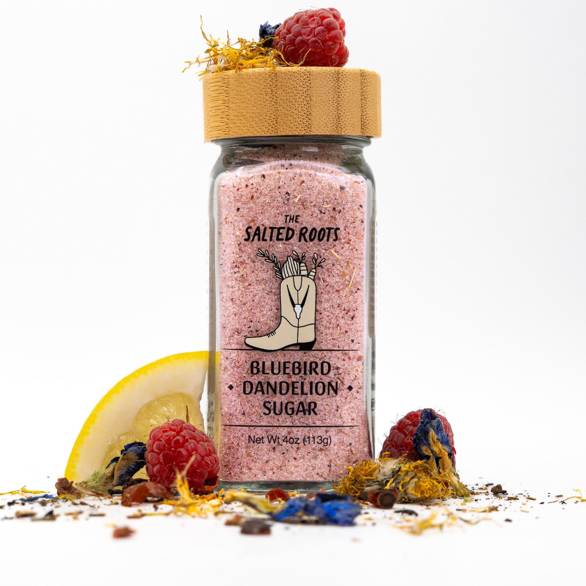 Glass salt jar with wooden lid and labels. Herbs, flowers, lemon, and raspberries scattered around jar. 
