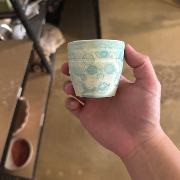A short ceramic shot glass with a bubble glaze effect. 