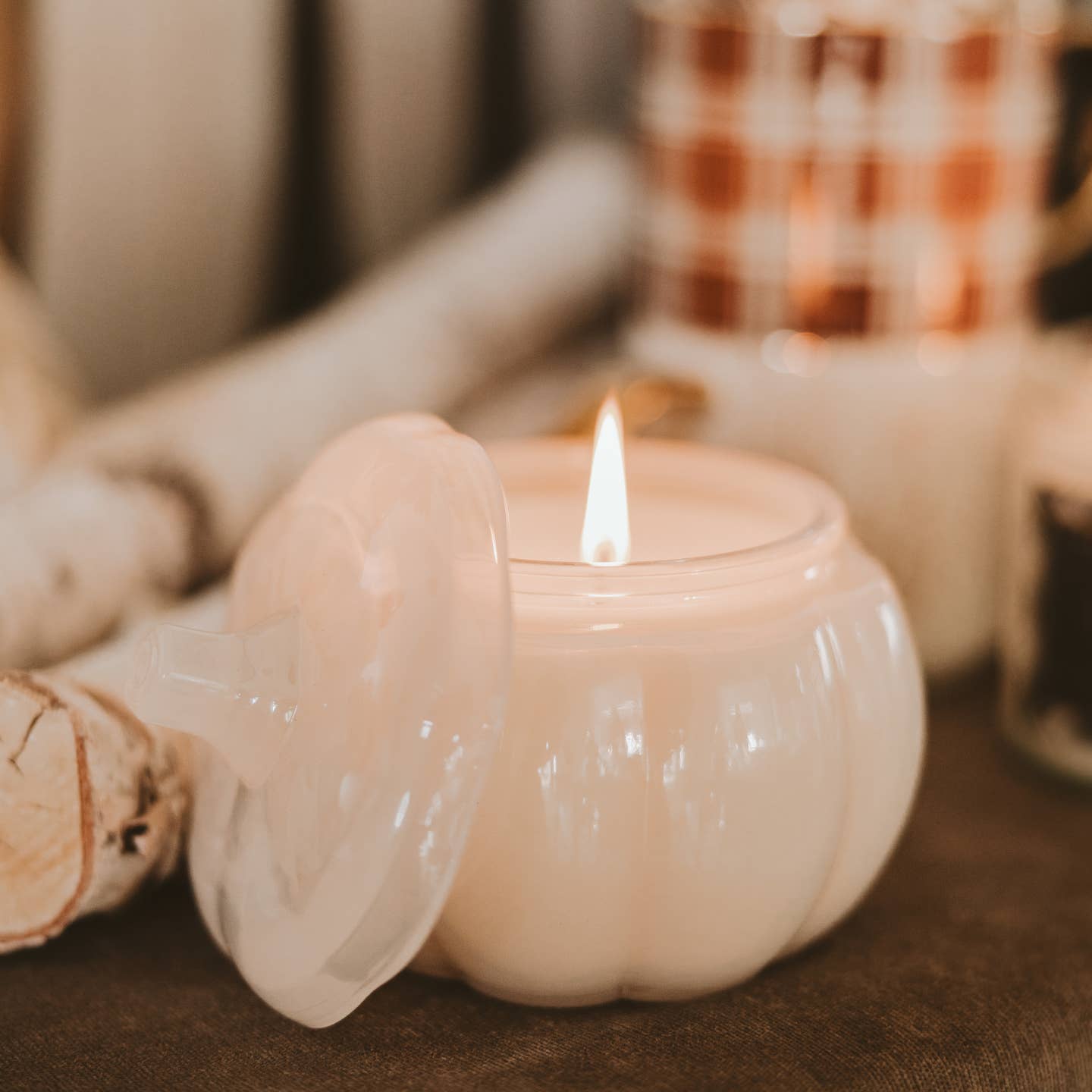 Pumpkin-shaped candle with a lit flame on a wooden surface.