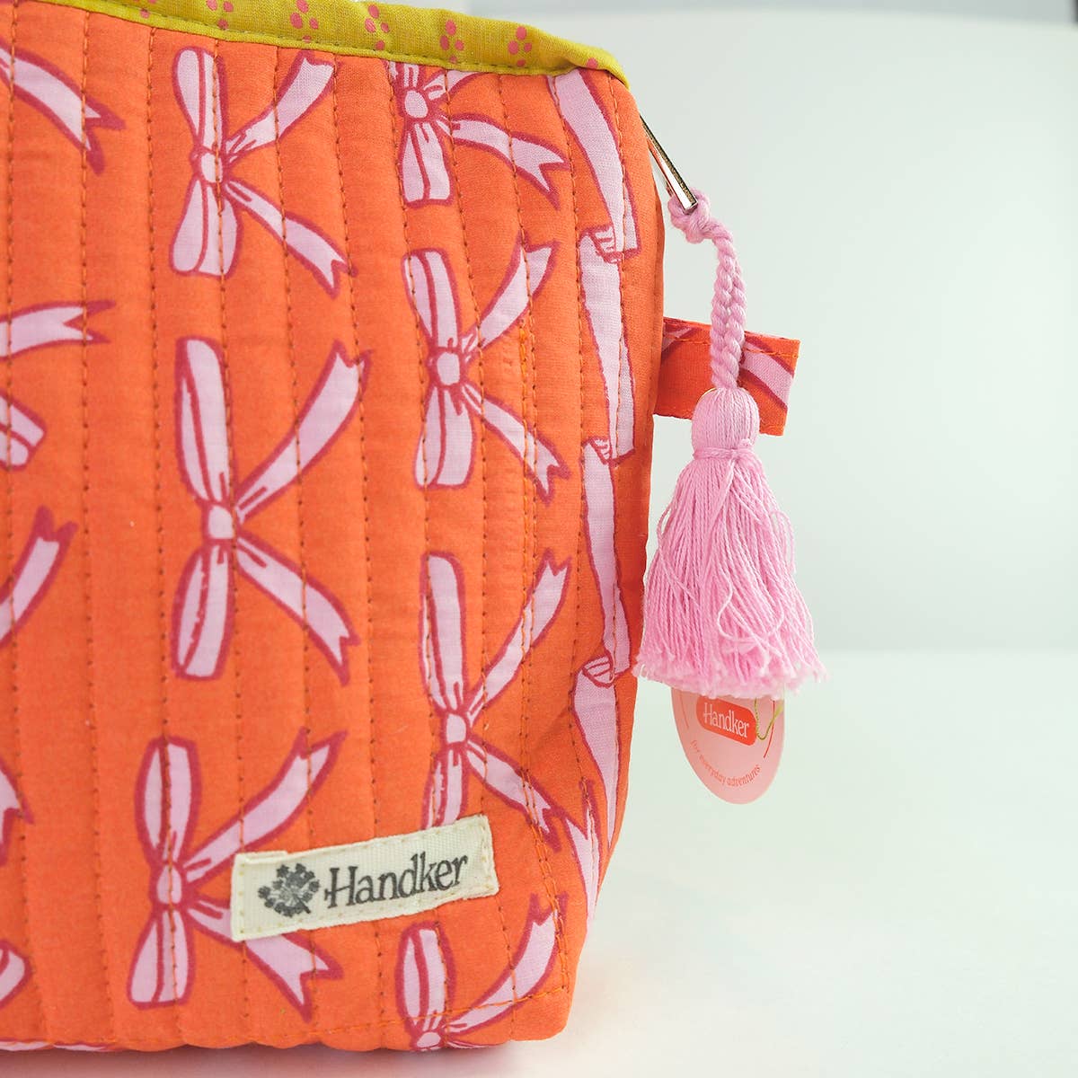 Orange pouch with pink bow pattern and tassel, featuring a 'Handker' brand label.