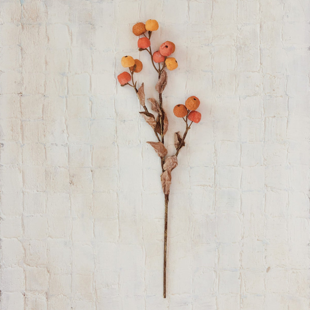 Artificial flower stem with orange berries on a textured beige background