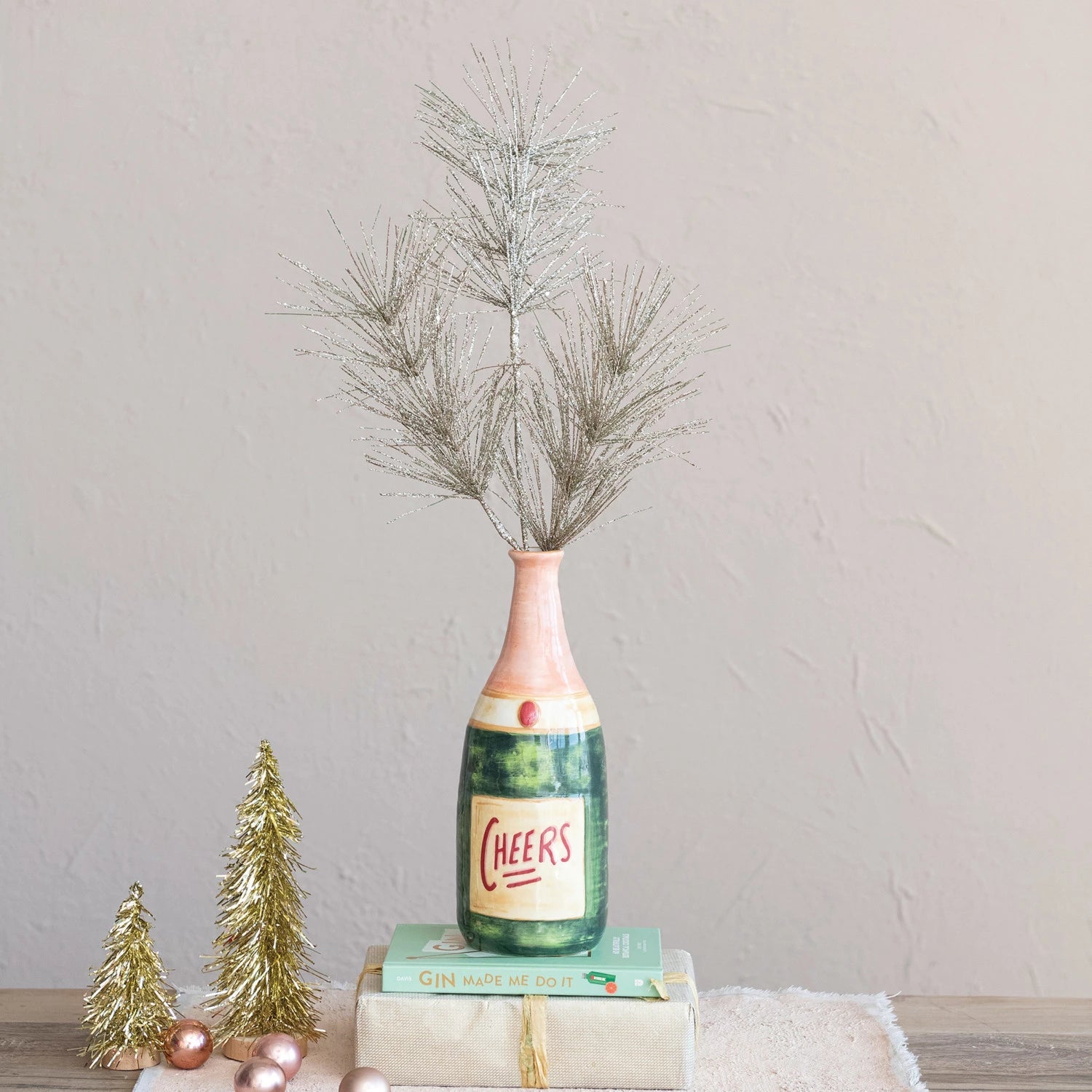 Decorative bottle with 'Cheers' label and greenery on a neutral background