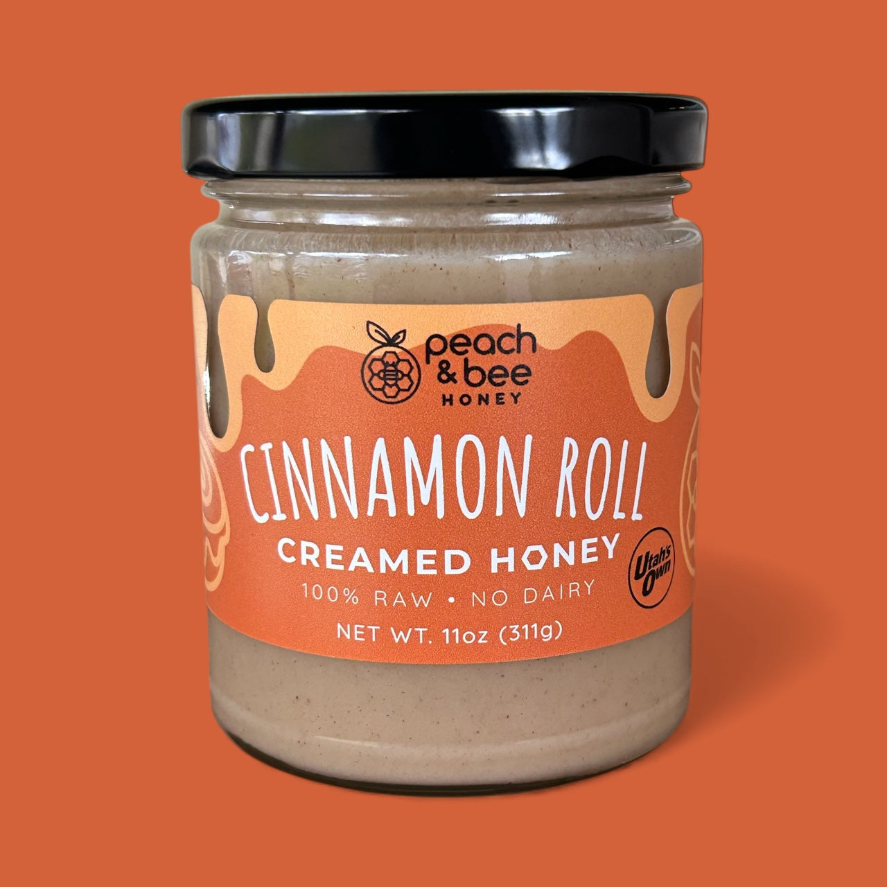 Jar of peach & bee honey cinnamon roll creamed honey on an orange background