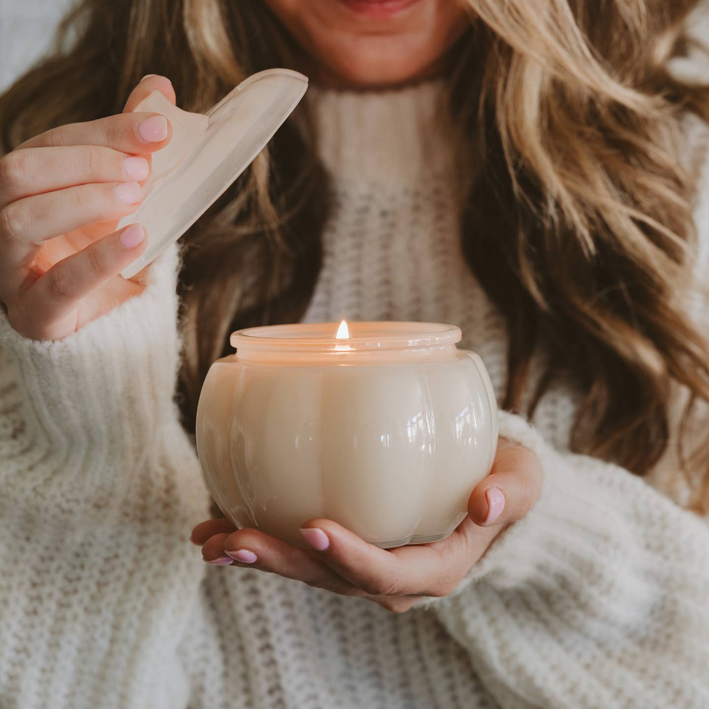 Person holding a lit candle in a white holder with a blurred background