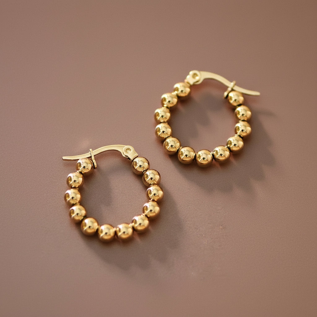 Elevate your everyday look with these 18K gold plated stainless steel hoop earrings, featuring delicate textured gold balls throughout. Measuring approximately 0.9" in length, they're the perfect size for versatile styling. Hypoallergenic and waterproof, these earrings resist tarnishing for lasting brilliance. To maintain their lustrous finish, avoid prolonged contact with lotions, perfumes, and cleaning products.
