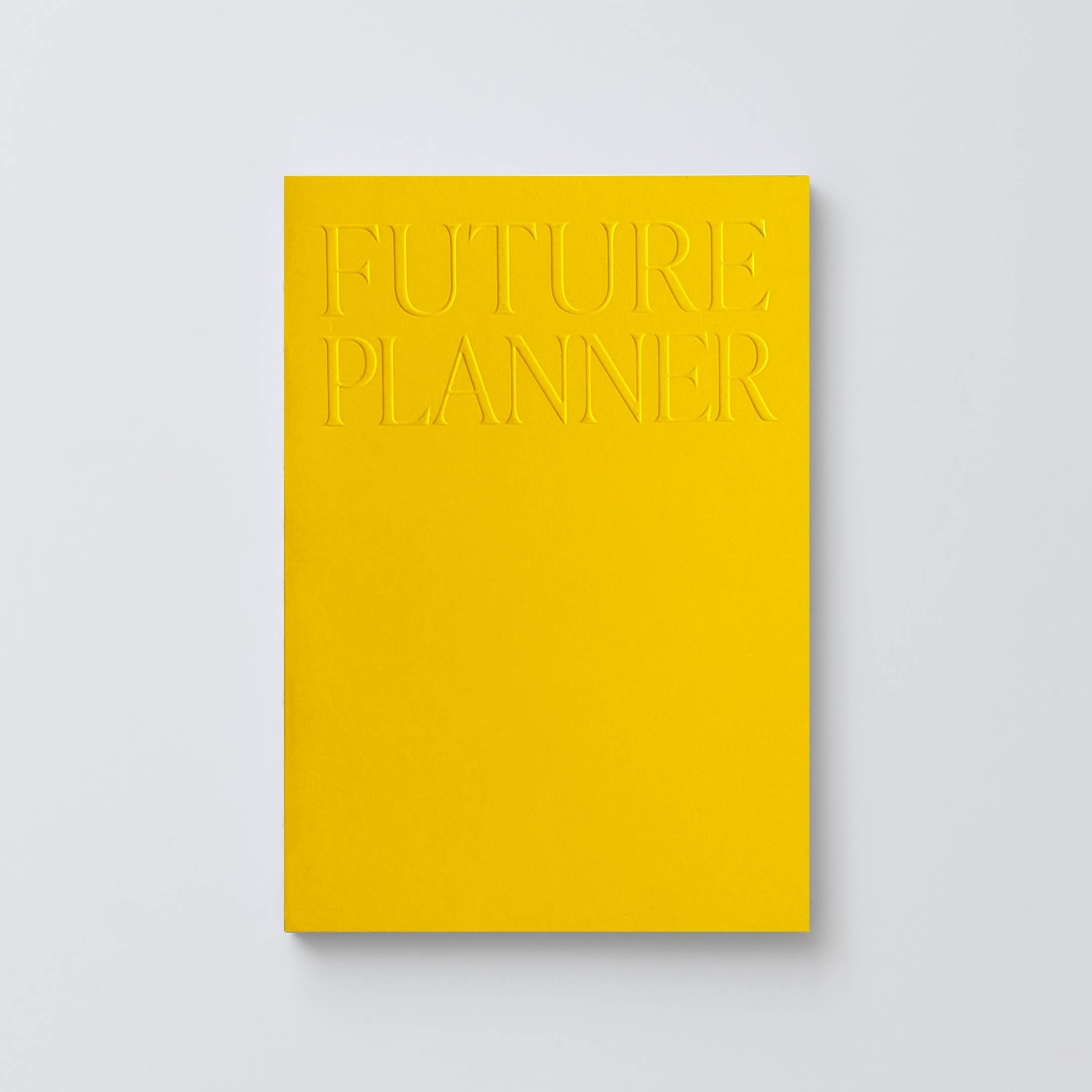 A minimalist yellow notebook or planner with embossed text reading 'FUTURE PLANNER' on the cover, shown against a light gray background.