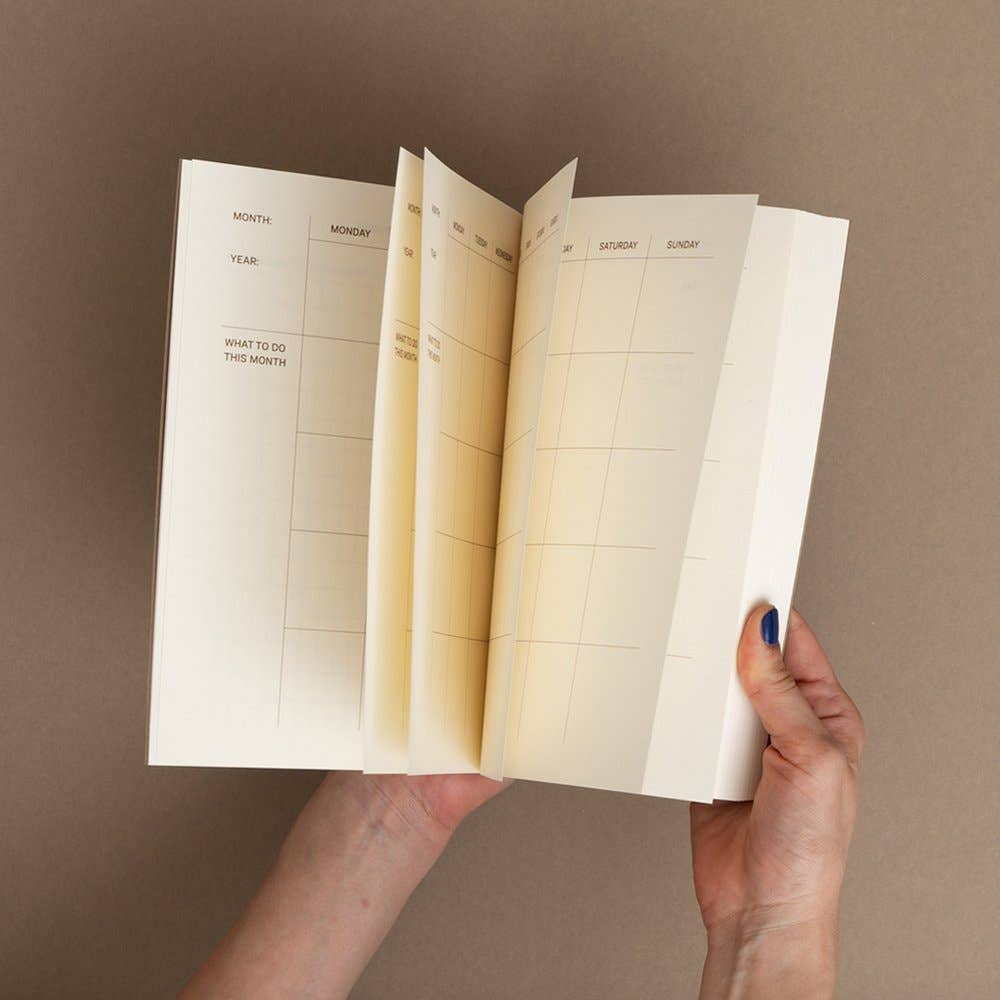Hand holding an open planner with grid layout on a brown background