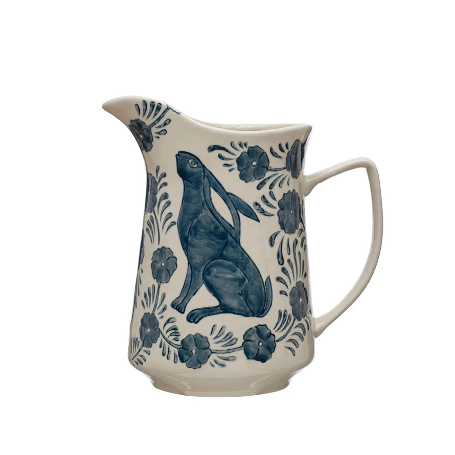 Serve up some whimsy with our Hand-Painted Stoneware Pitcher in charming blue and white. This pitcher features a playful rabbit and flower design, making it a delightful addition to any kitchen or dining table. Hand-crafted and hand-painted, each pitcher is unique and adds a touch of personality to any setting.