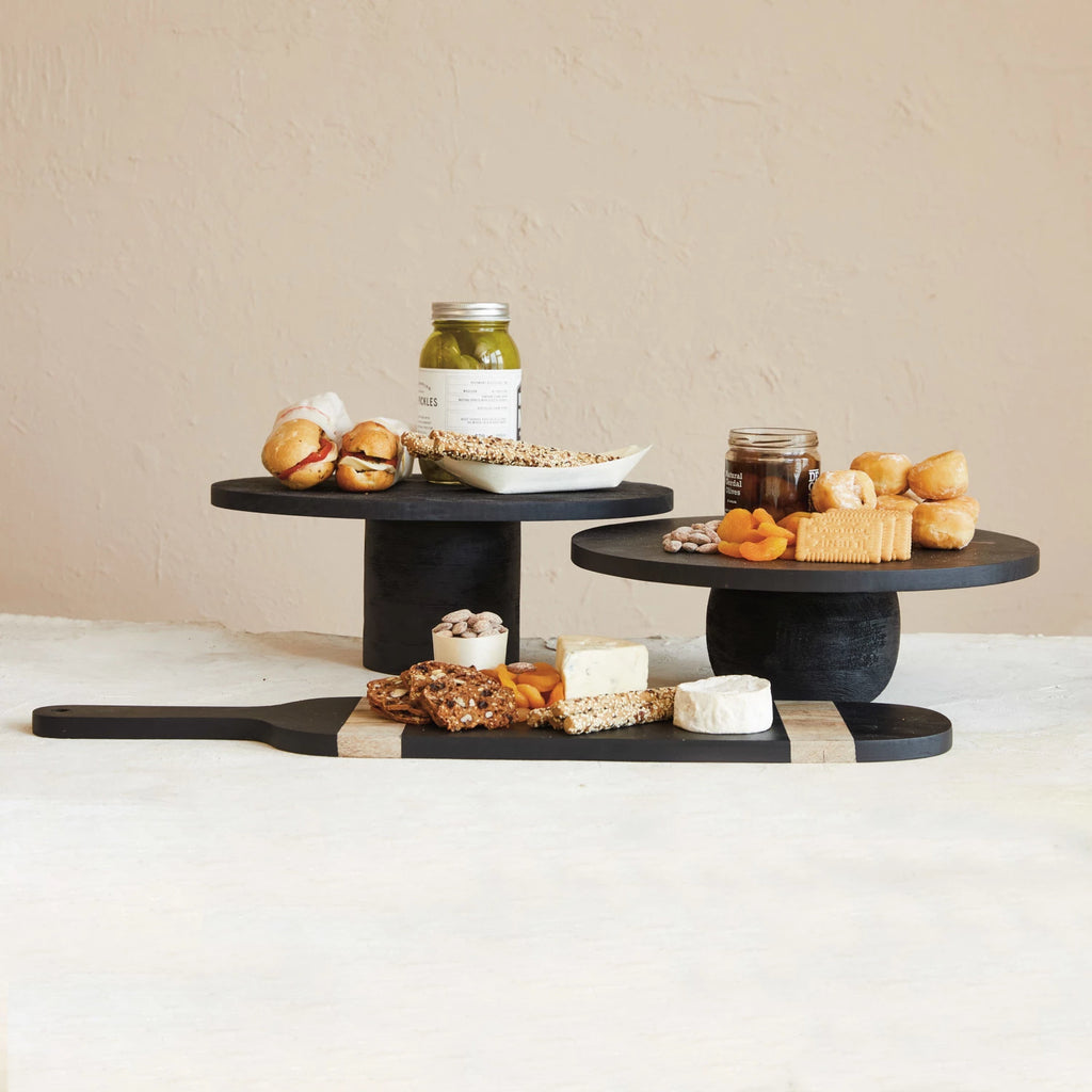 This black mango wood pedestal is a wonderful way to add height and elegance to the home. The pedestal is made of mango wood painted black and polished to create a smooth, shiny surface. The pedestal has an oval shape ideal for elevating or displaying cakes, pies, or other desserts that suit any farmhouse, French country, lodge, or Scandinavian home.