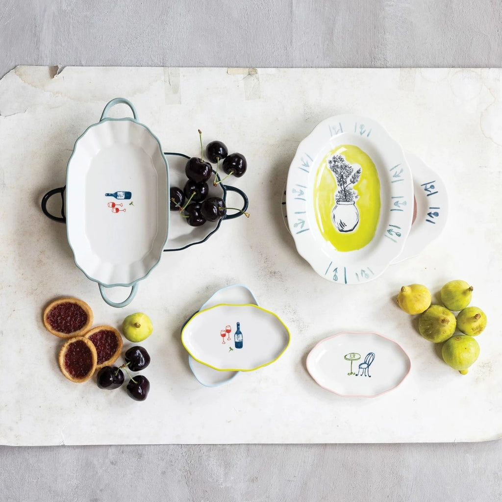 Add some quirky charm to your kitchen with our Hand-Painted Stoneware Dish featuring a colorful rim and bistro image. Each dish is unique and adds a touch of personality to your table. Available in 4 styles, it's the perfect dish for any meal. 