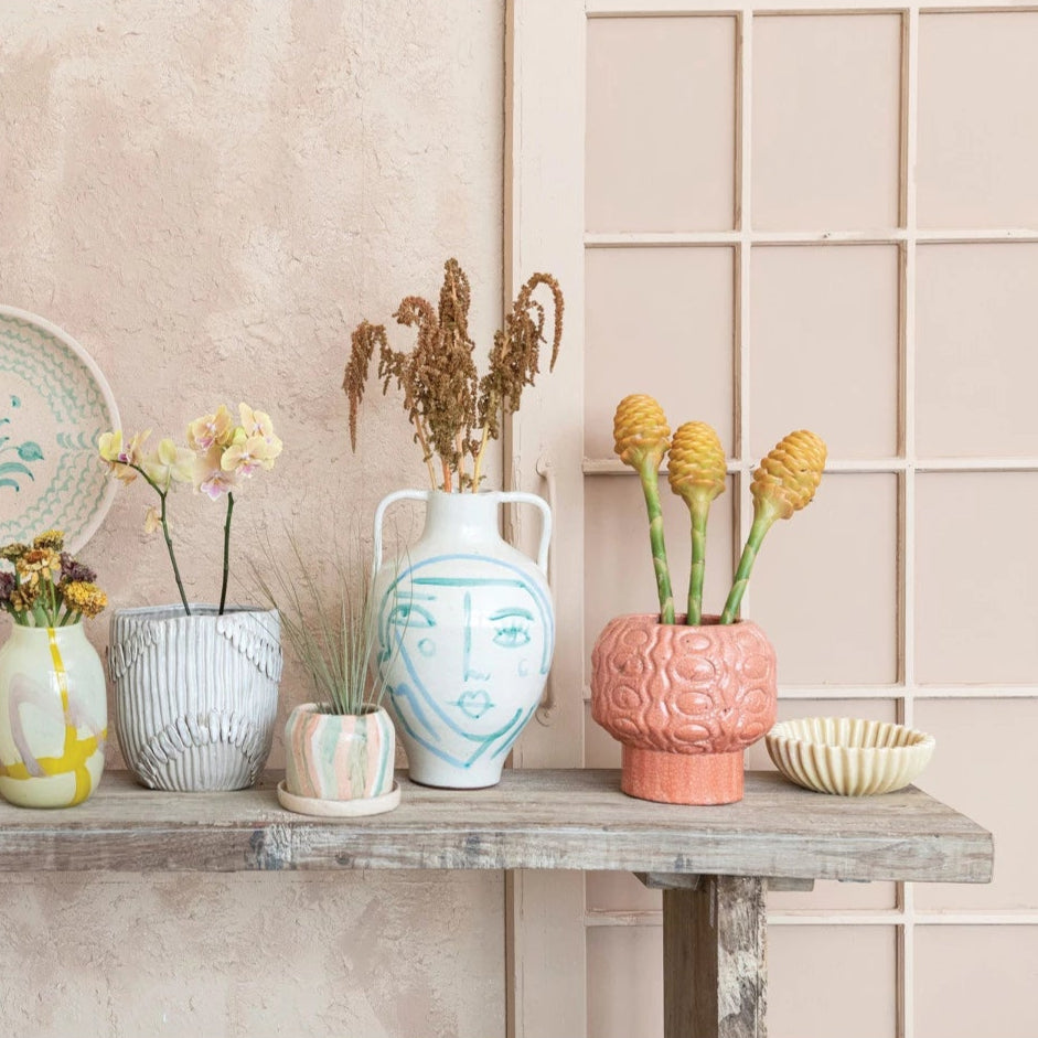 This hand-painted terra-cotta vase features an abstract face and crackle glaze in white, blue, and aqua colors. It is a unique and beautiful home accessory, made of baked clay with a porous and earthy texture. The vase has a round shape and wide opening, and its hand-painted design adds a playful and artistic touch. The crackle glaze creates a glossy surface, while the white, blue, and aqua color scheme adds a cozy and elegant look.