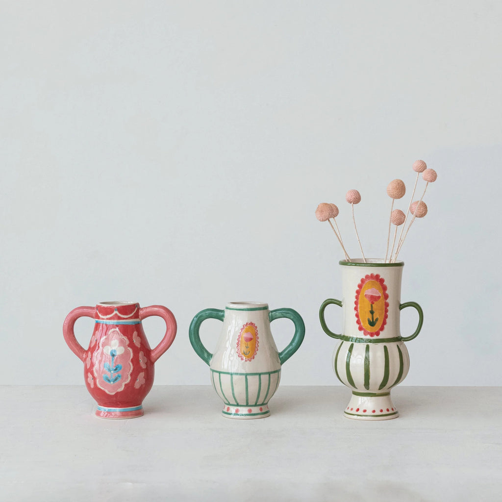 This Hand-Painted Stoneware Urn with Flower, Stripes, and Handles is a celebration of artistry and color. Its multi-colored palette includes a range of hues that complement its unique design. The urn's other shape sets it apart, offering a fresh take on traditional vases. Influenced by Scandinavian, Boho, and French Country styles, it serves as a versatile decor piece