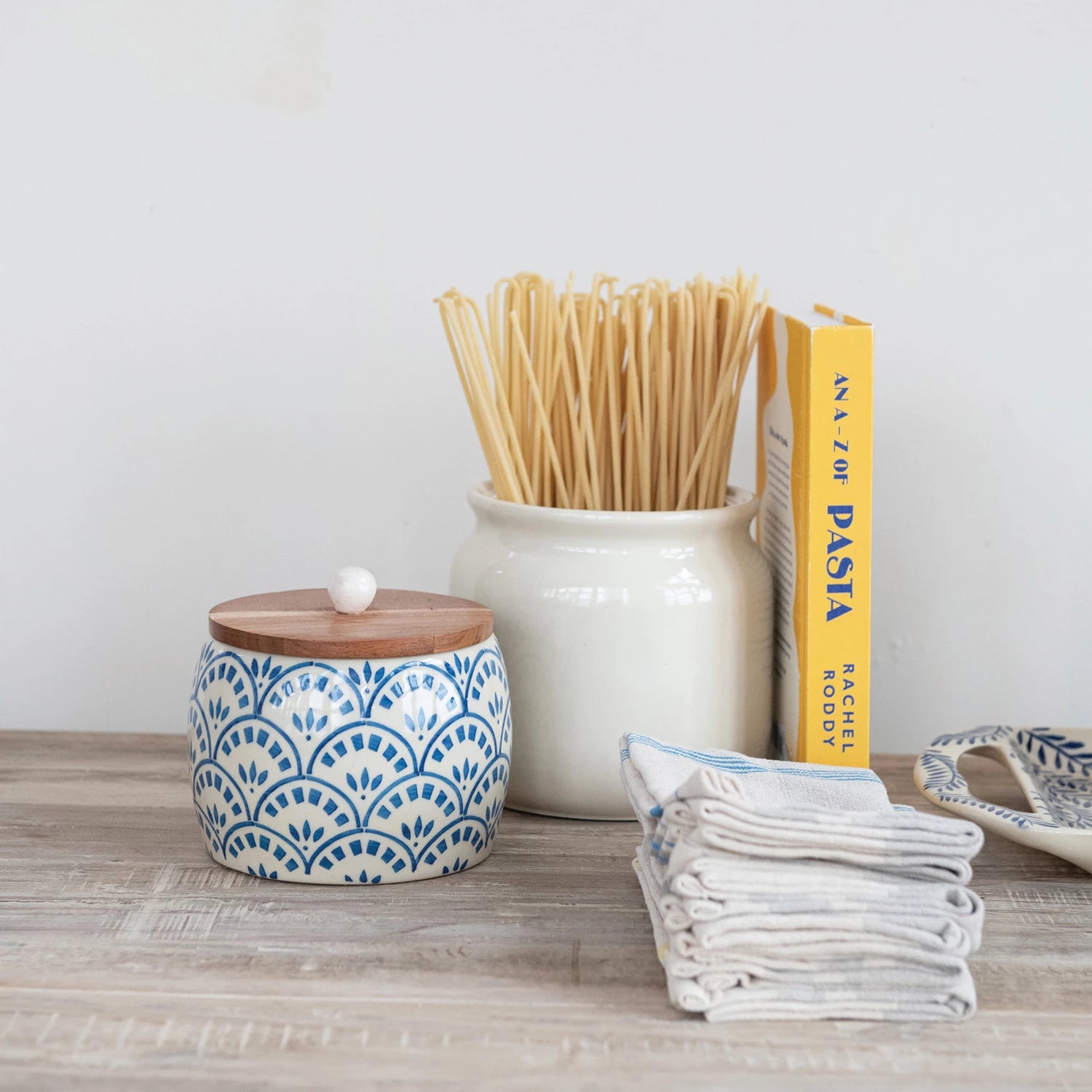 Brighten up your kitchen with this Hand-Painted Stoneware Canister topped with a warm Acacia Wood Lid! Perfect for storing everything from coffee to cookies, its unique hand-painted design adds a splash of personality to your countertop. The natural wood lid keeps contents fresh while giving your space a cozy, playful vibe. Storage has never looked this fun! 5-3/4" Round x 5-1/4"H