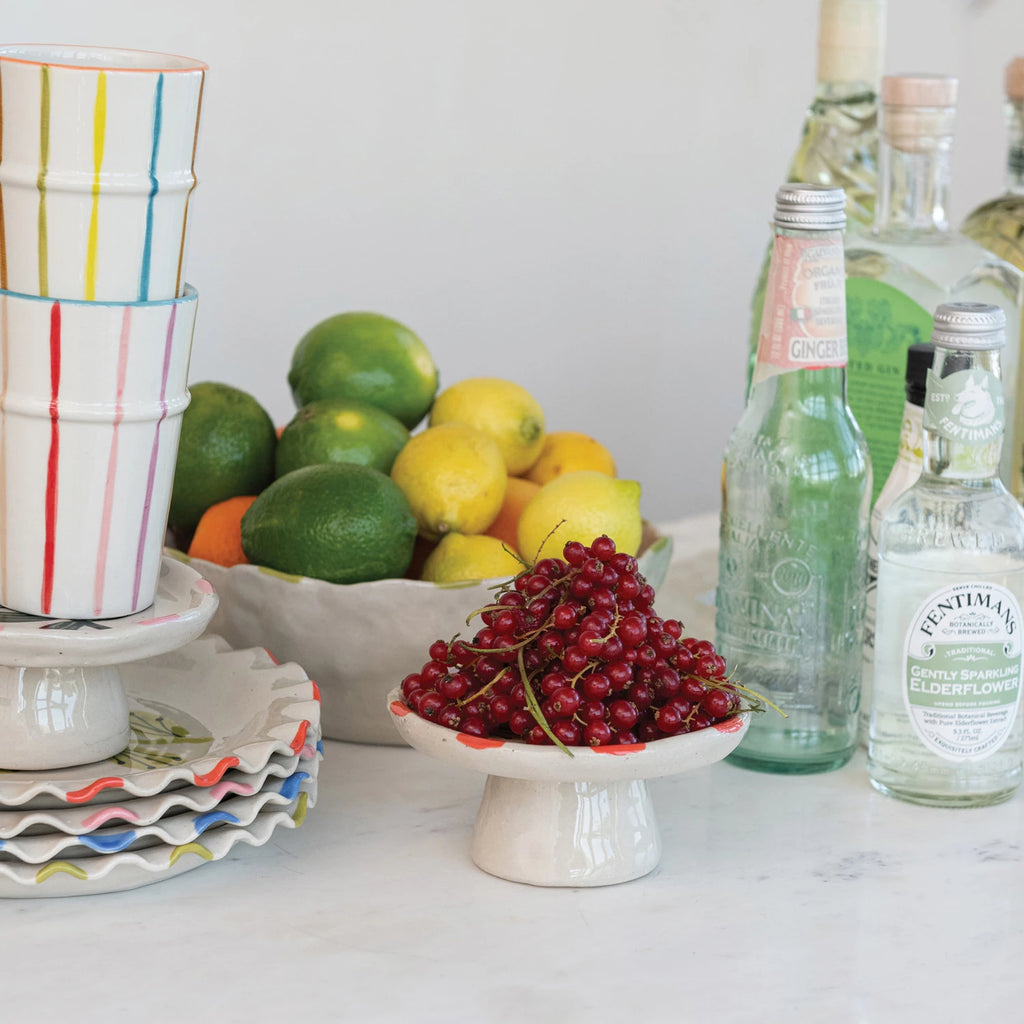 Add a splash of charm to your table with this Hand-Painted Stoneware Pedestal featuring a delightful pink flower &amp; green leaf design. Perfect for showcasing desserts or elevating your favorite treats, its sturdy stoneware build combines beauty and function. Brighten up any gathering with this playful centerpiece that’s as practical as it is pretty!&nbsp;5" Round x 2-1/2"H