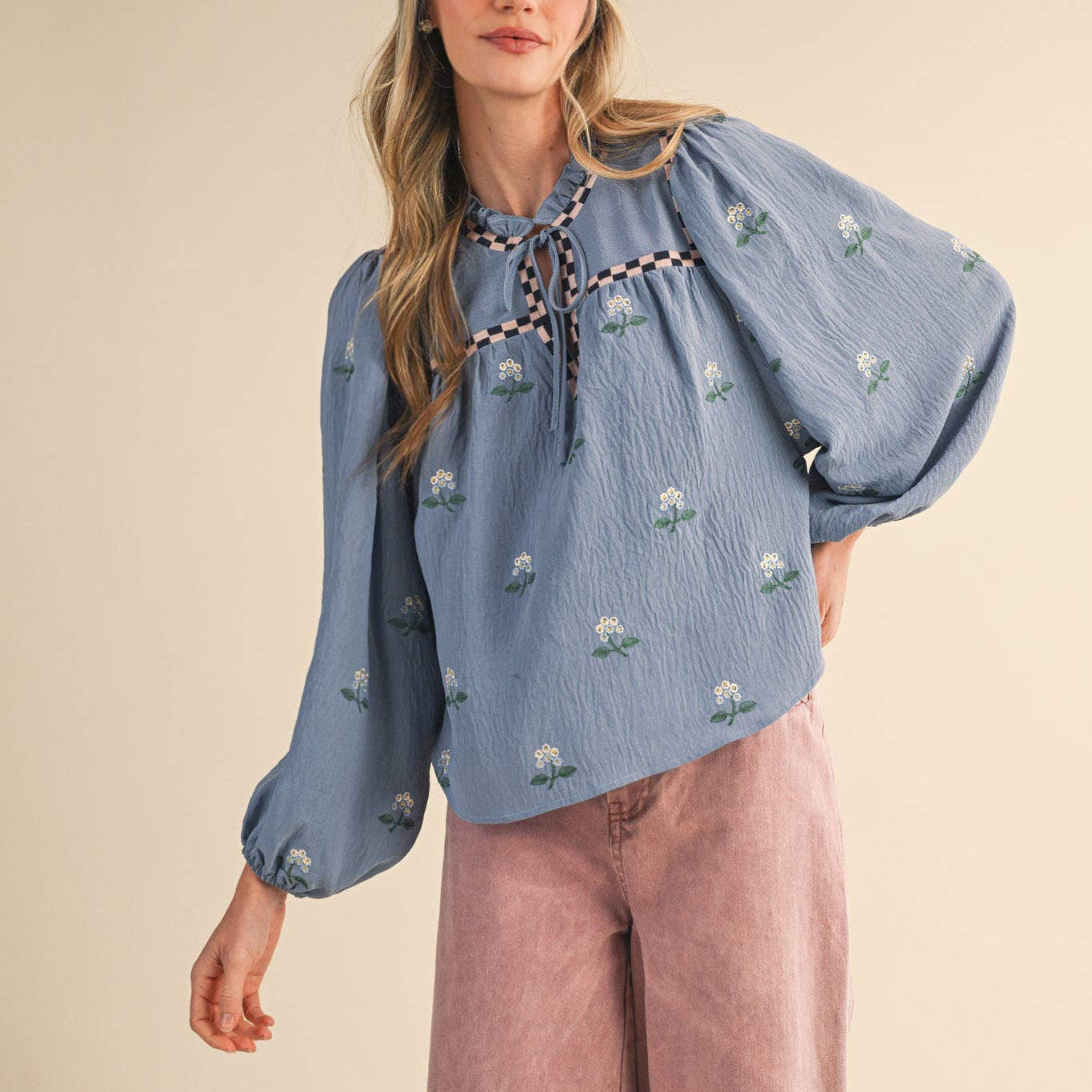 Embrace effortless charm with this enchanting floral embroidered babydoll top in soft dusty blue. The delicate all-over floral embroidery paired with checkered details on the neckline and yoke creates a romantic, thoughtfully designed piece that celebrates feminine style. The ruffled neckline features a sweet keyhole opening with tying detail, while long balloon sleeves with elastic cuffs offer a flattering, comfortable fit. Fully lined for confidence and ease.