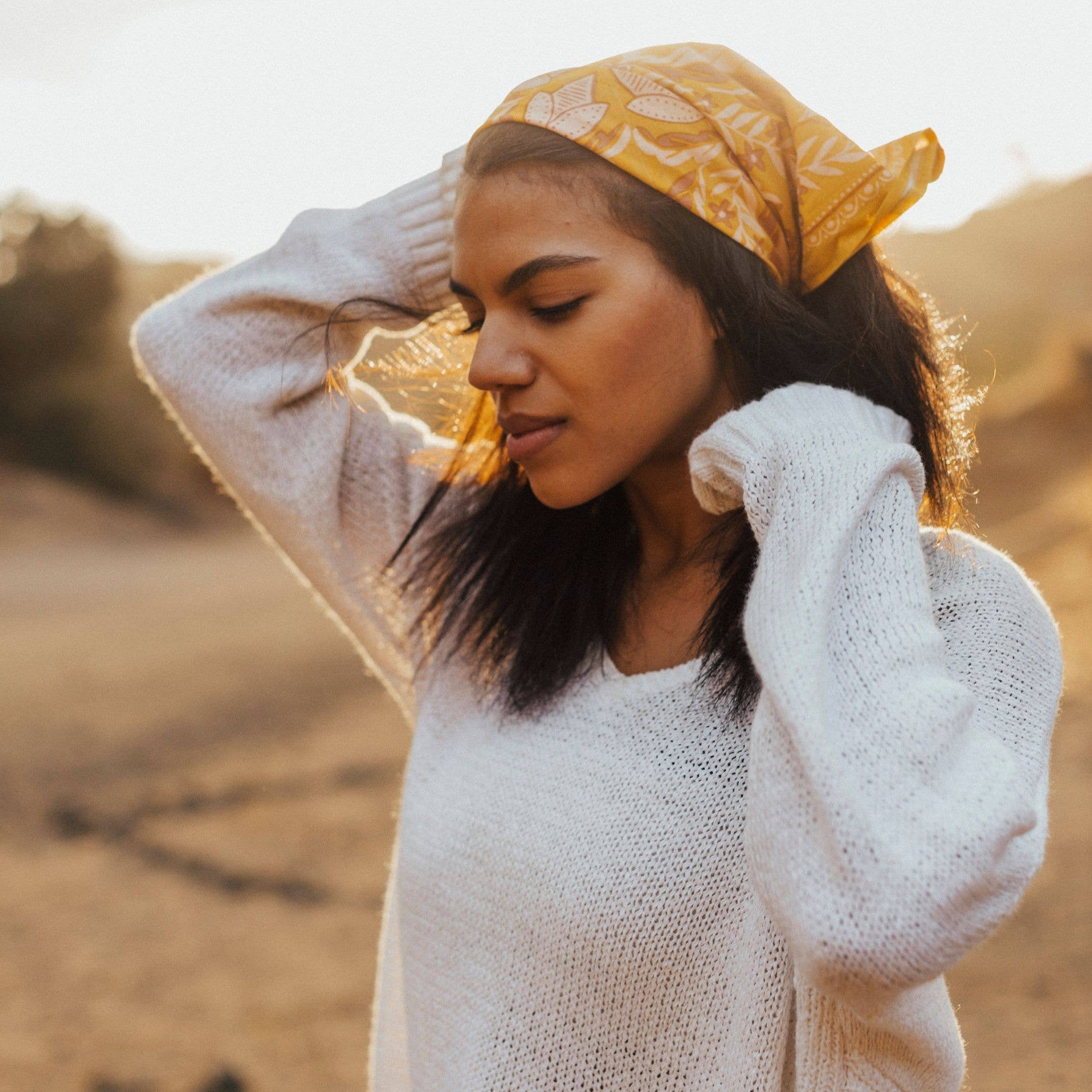Woman wearing a yellow headscarf and white sweater in a desert setting