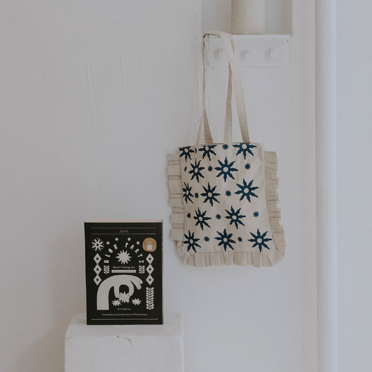 Tote bag with star pattern hanging on a white wall next to a black book.