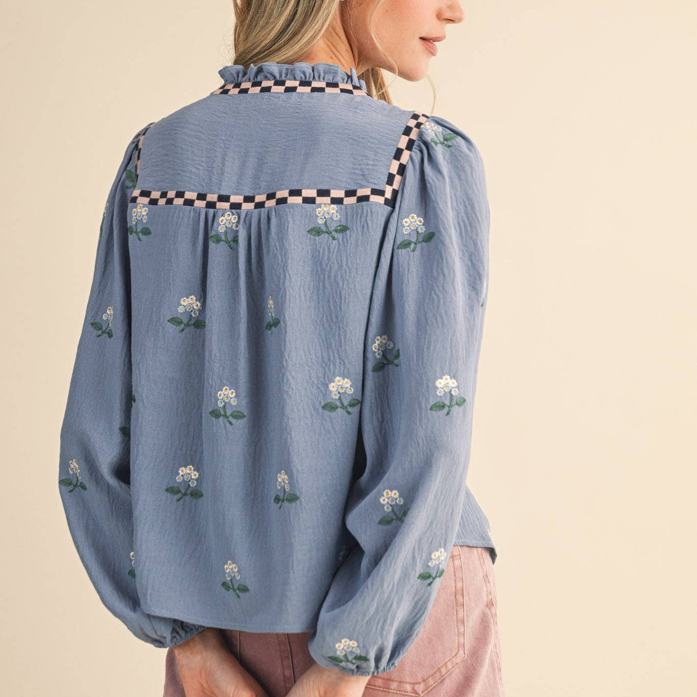Embrace effortless charm with this enchanting floral embroidered babydoll top in soft dusty blue. The delicate all-over floral embroidery paired with checkered details on the neckline and yoke creates a romantic, thoughtfully designed piece that celebrates feminine style. The ruffled neckline features a sweet keyhole opening with tying detail, while long balloon sleeves with elastic cuffs offer a flattering, comfortable fit. Fully lined for confidence and ease.