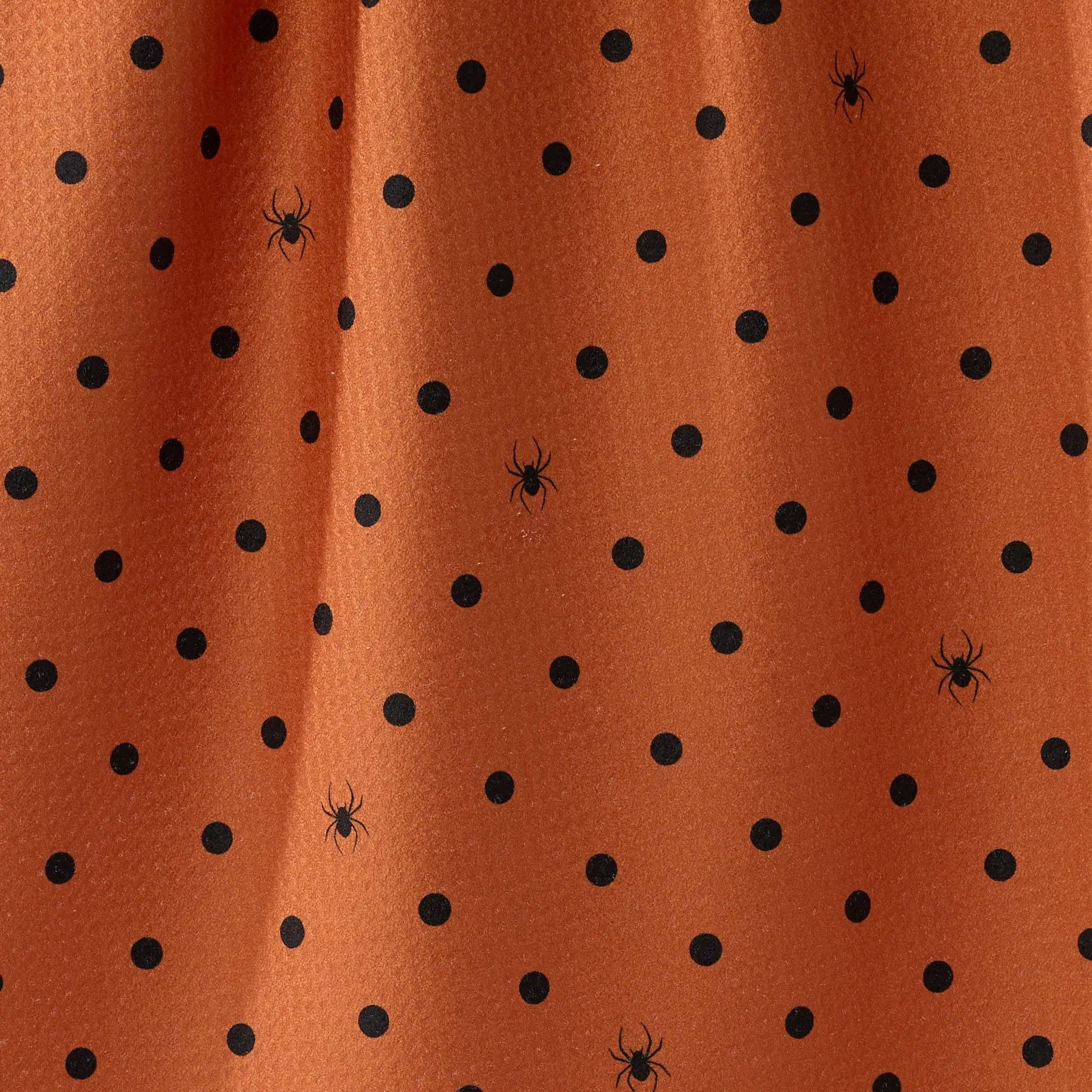 Close-up of an orange tea towel with a black polka dot pattern and small spider motifs.