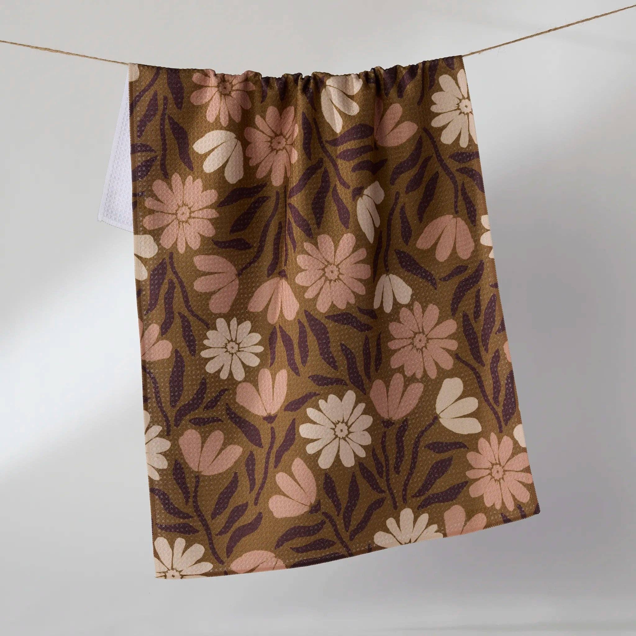 A TEA TOWEL with a retro floral pattern in brown, beige, and pink, hanging from a thin wire against a plain light gray background.