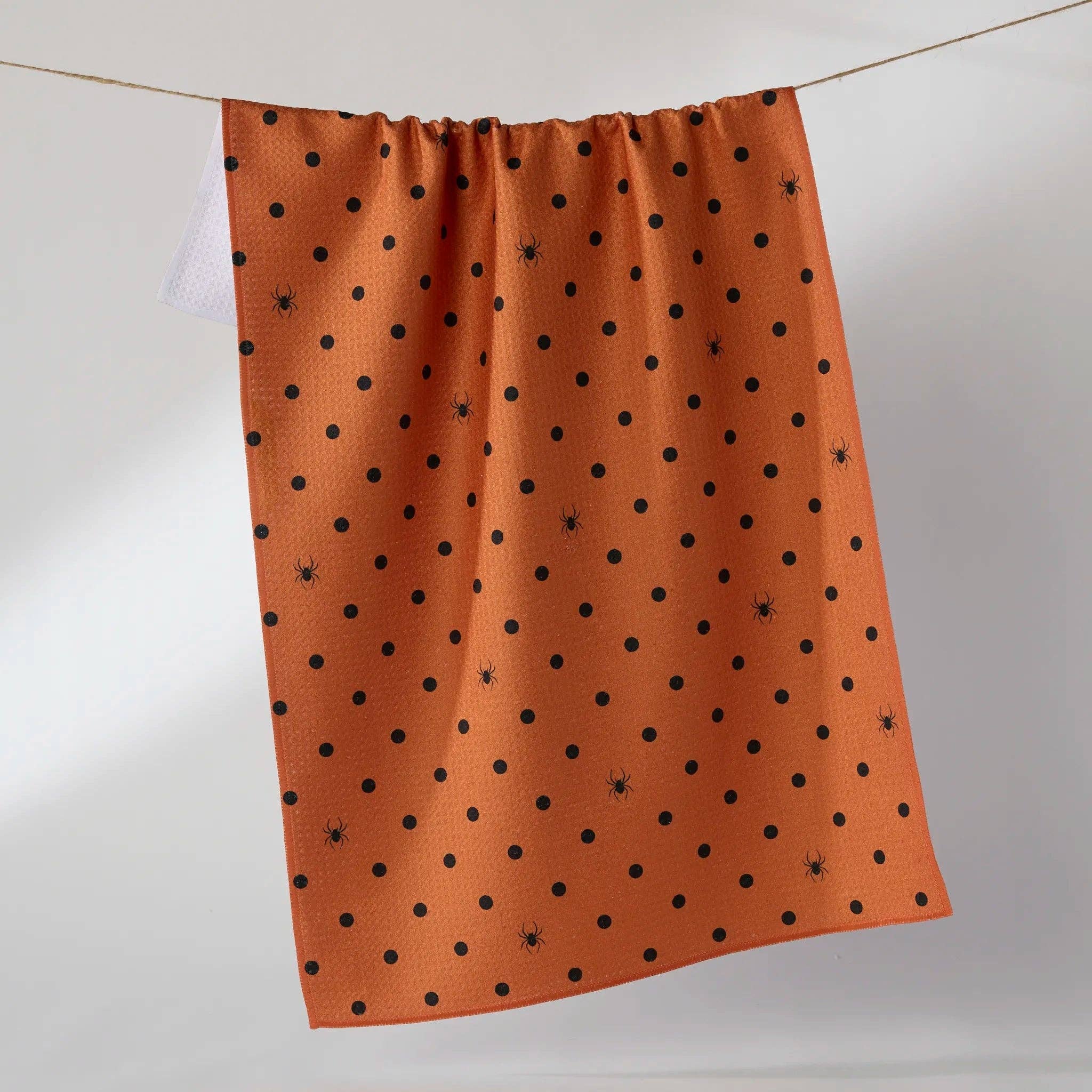 An orange tea towel with a black polka dot pattern, hanging from a thin wire against a light gray studio background.