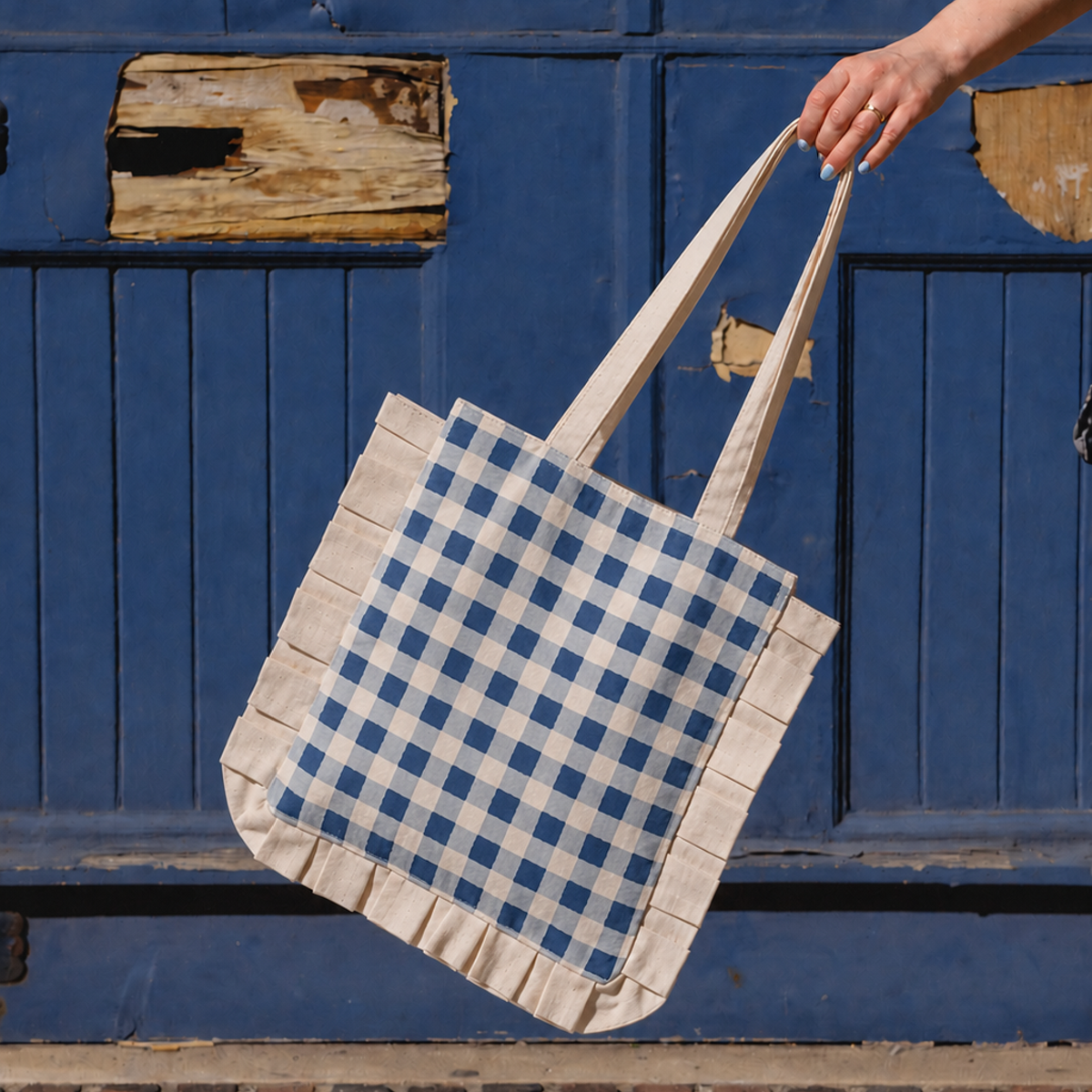 Tote bag with blue and white checkered pattern held by a hand against a blue wooden background