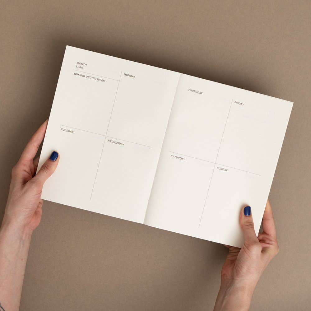 Person holding a white planner with days of the week on a beige background