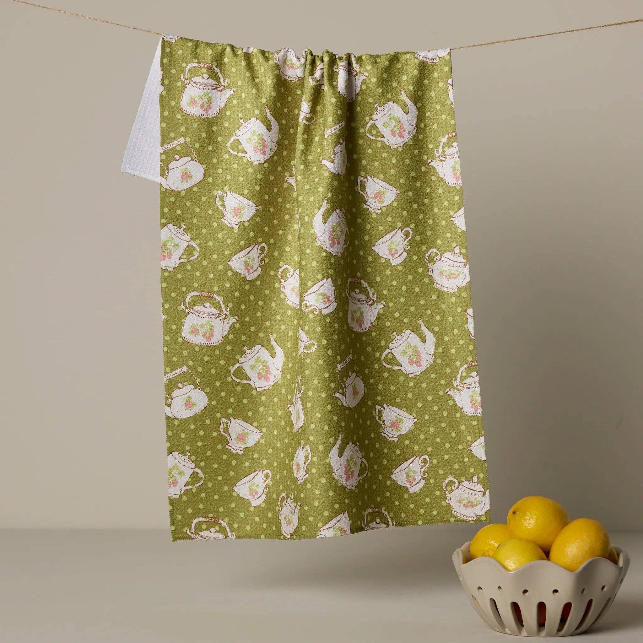 Green tea towel with white teapot pattern hanging on a line, next to a bowl of lemons.