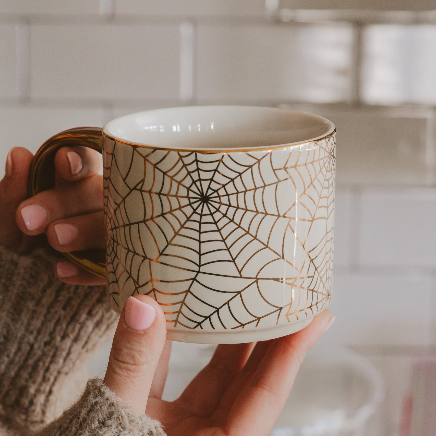 Person holding a mug with a spider web pattern in a kitchen setting