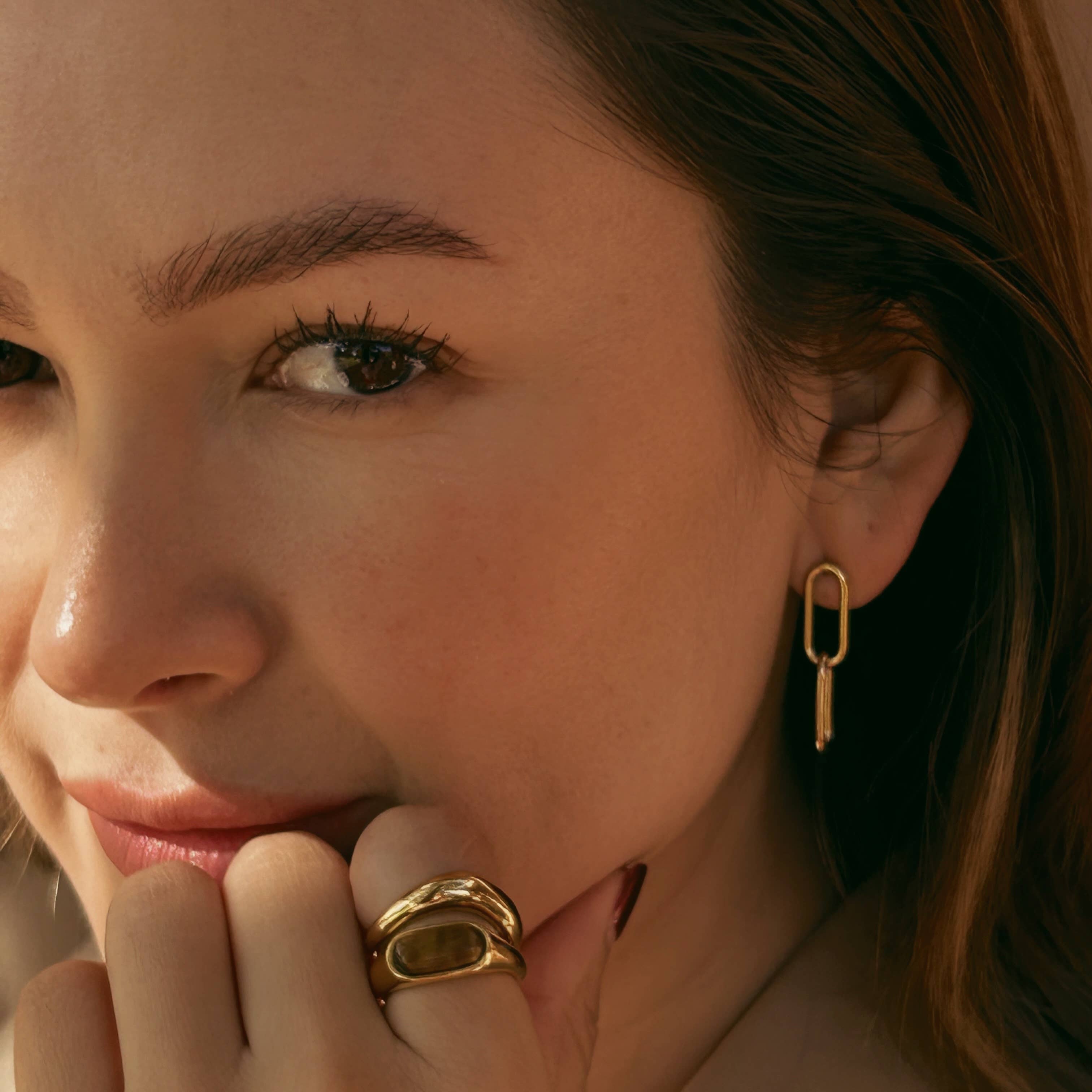 Close-up of a woman wearing gold earrings and ring, with a soft focus on her face.