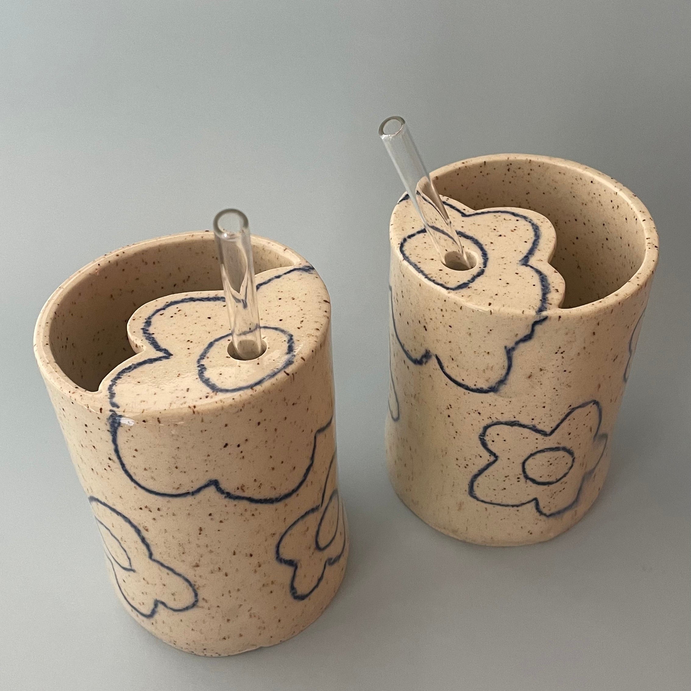 ceramic travel mugs with dark blue flower details and a flower shaped lid with a straw hole