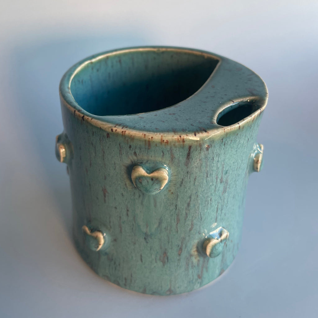 ceramic aqua travel cup with a sipper top and hearts around the sides