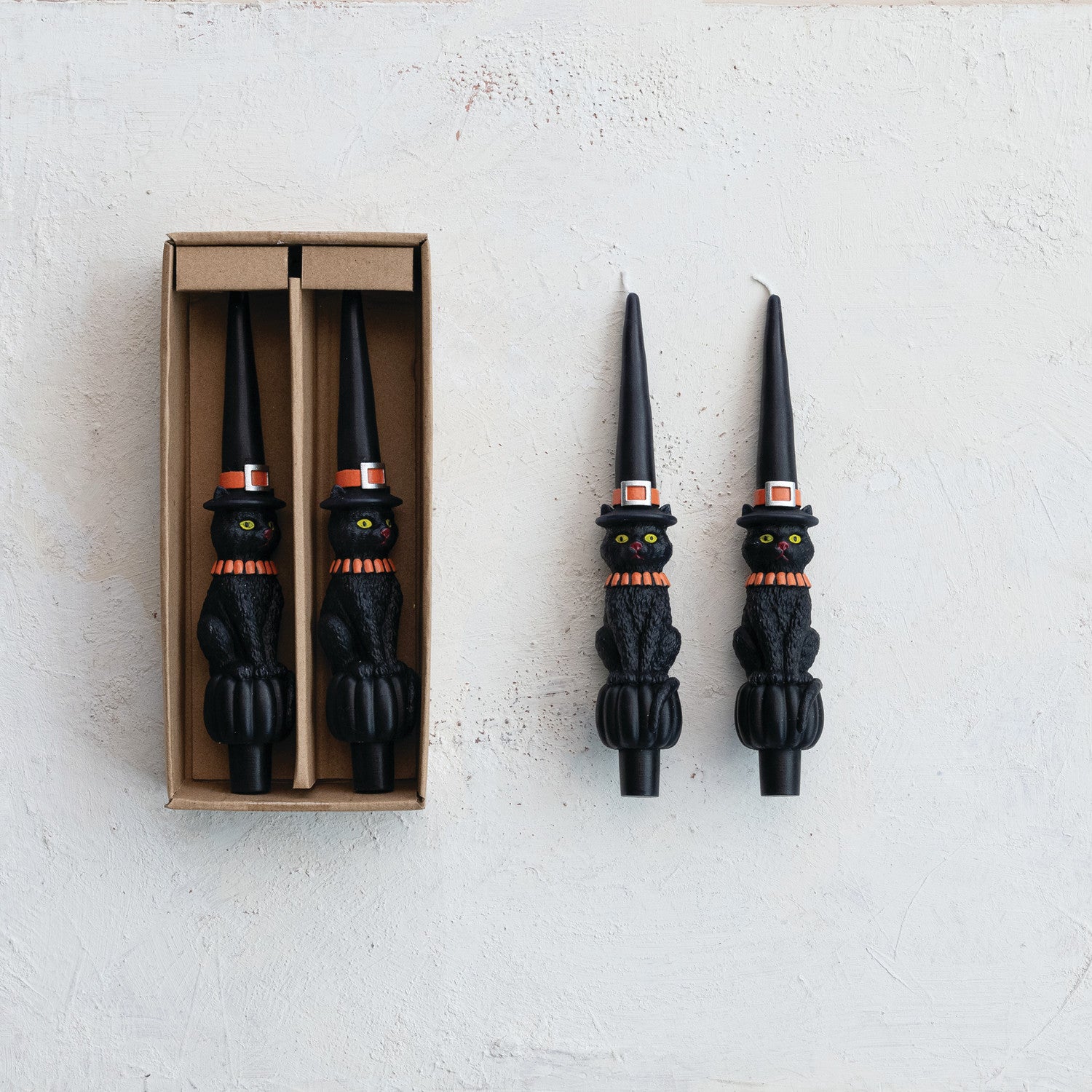 Black cat-shaped candles with decorative hats on a white background