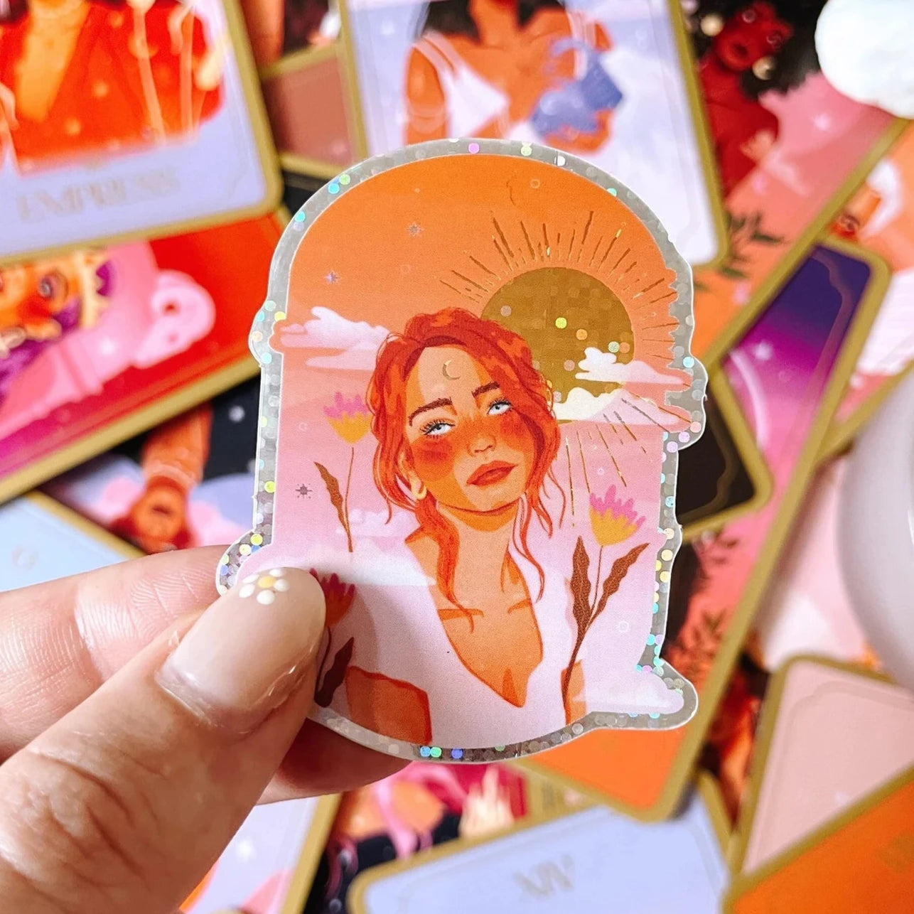 A white woman with red hair stares into the distance. She has her hair in a messy updo with pieces framing her face. She is wearing a plain top with a v neck. On her forehead is a crescent moon and behind her is a glittering sun. 