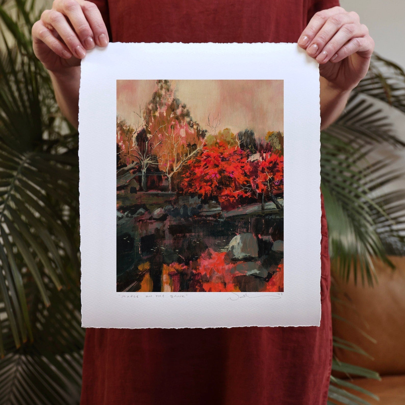 print held by woman against a leather couch and fern. 