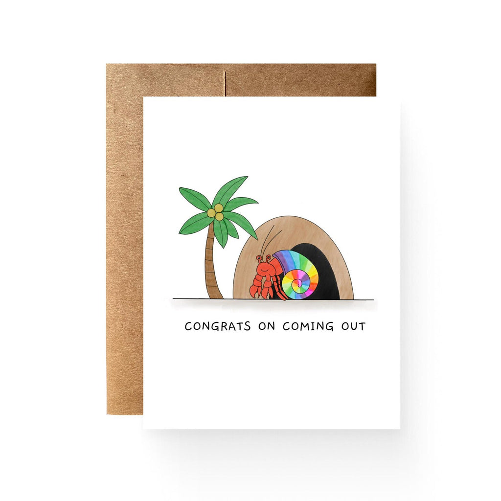 white card with a cave, palm tree, and hermit crab with a rainbow shell. reading "congrats on coming out"