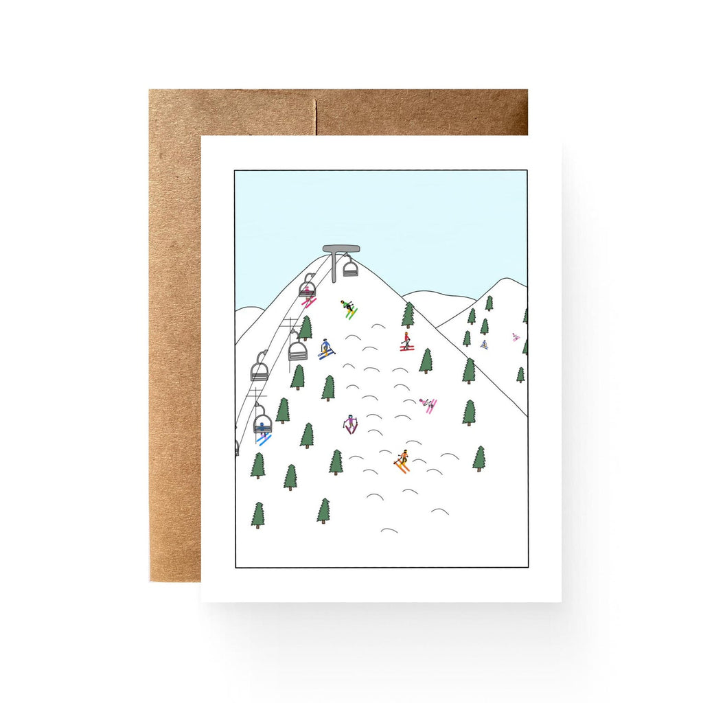 card with a ski lift and skiers on a mountain top covered in snow and pine trees