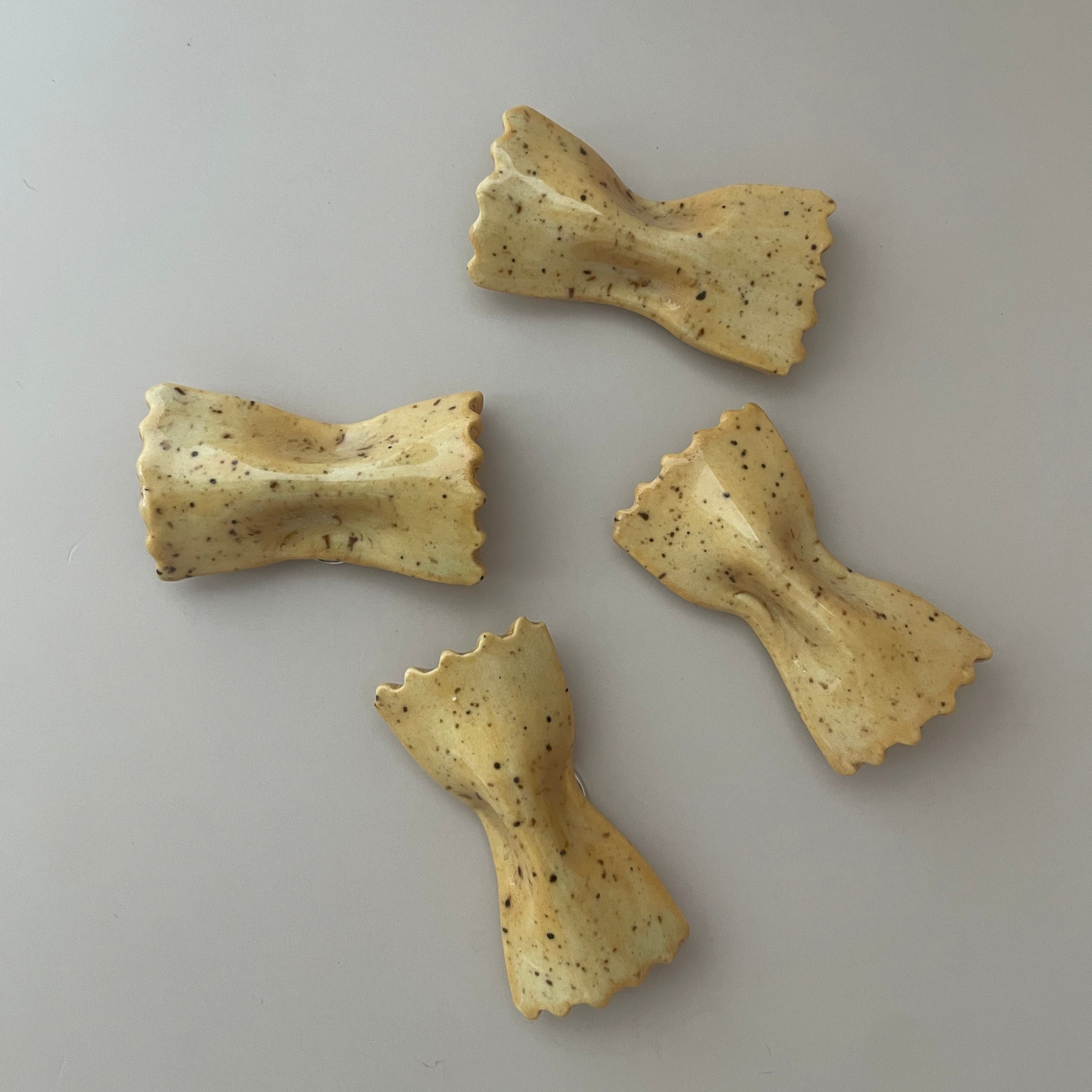 bowtie pasta shaped magnet with a pale yellow glaze and brown specks