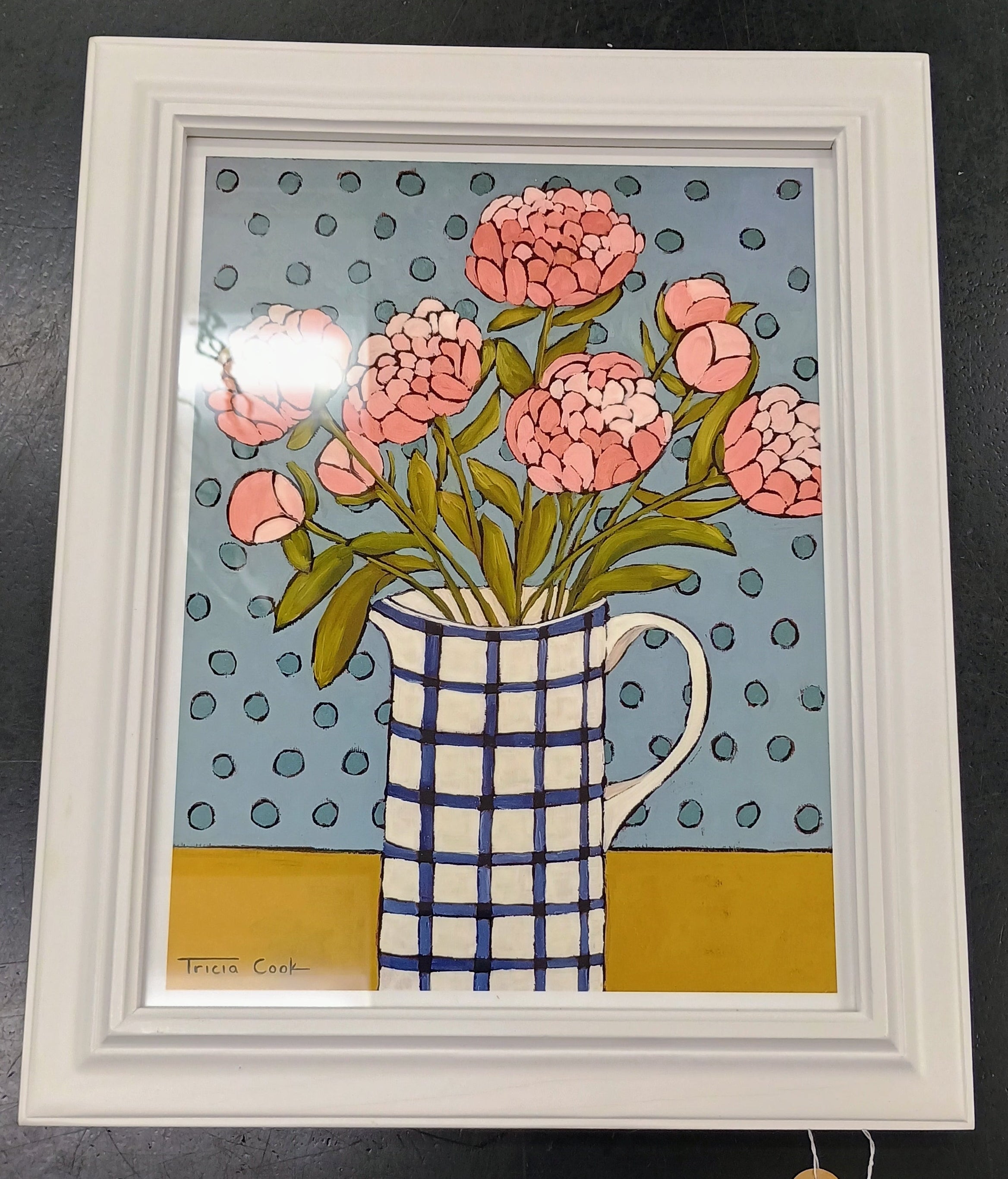 Framed Print with pink peonies in a blue white grid patterned pitcher, on a gold table top, with medium blue polka dots on a light blue background.  White Frame