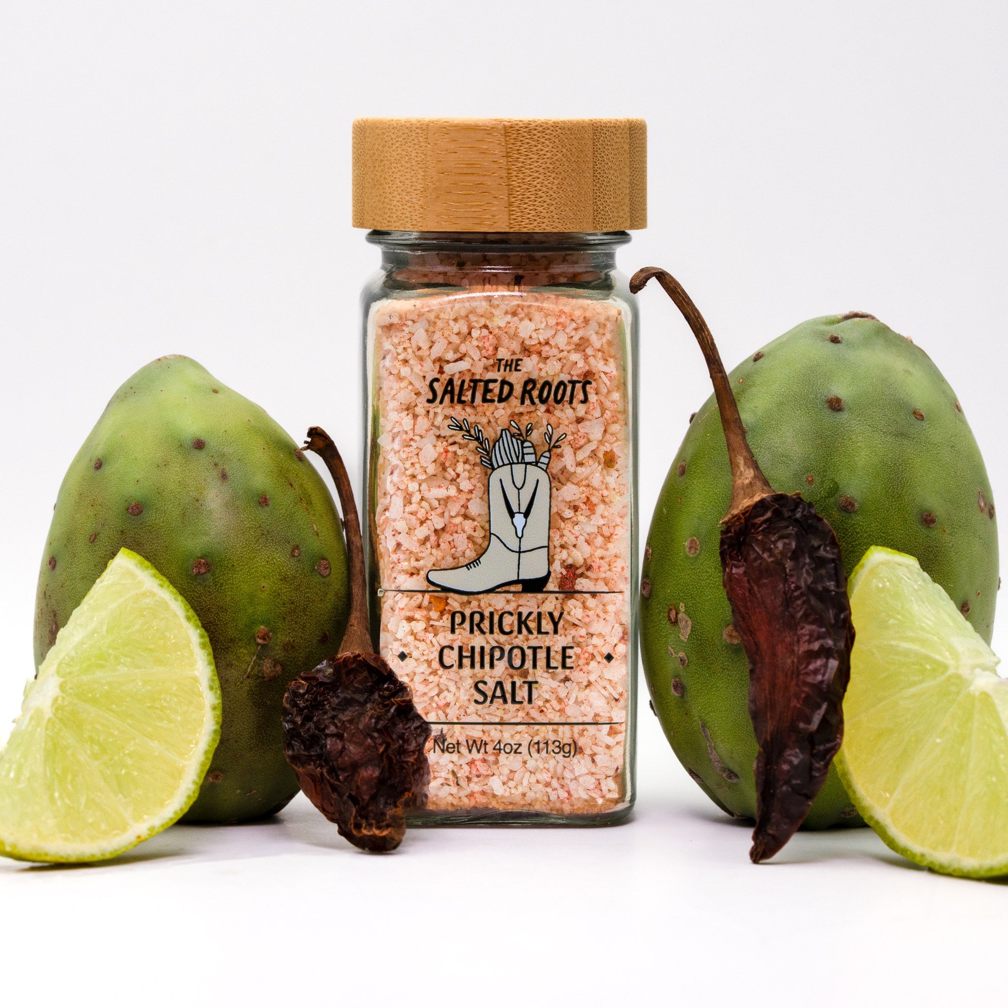Jar of salt with wooden lid and label. Lime, dried pepper, and cacti set around bottle. 